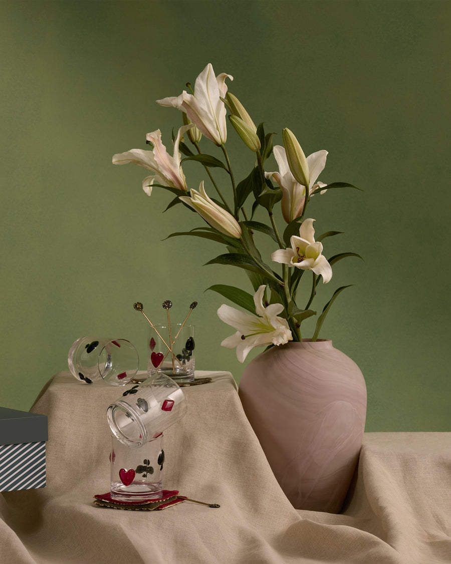 A Mehfil glass with card suits on a table with lilies in a clay vase