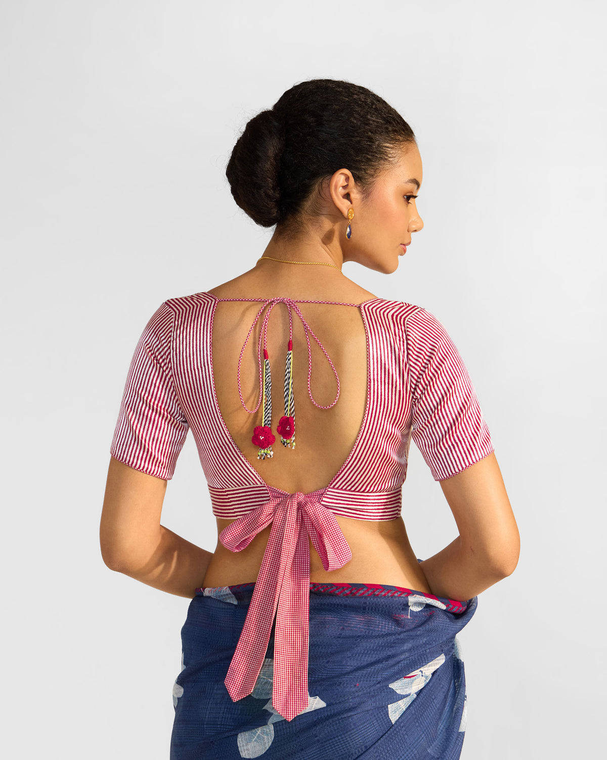 Back of a red and white striped Zahra Blouse with a tassel tie worn by a person.