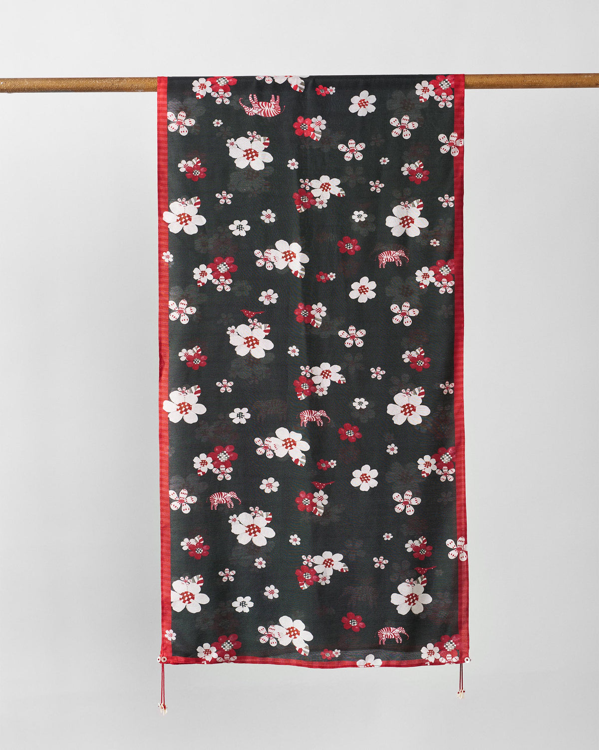 Fleur Scarf in red and black with white blossoms, hung from a rod.