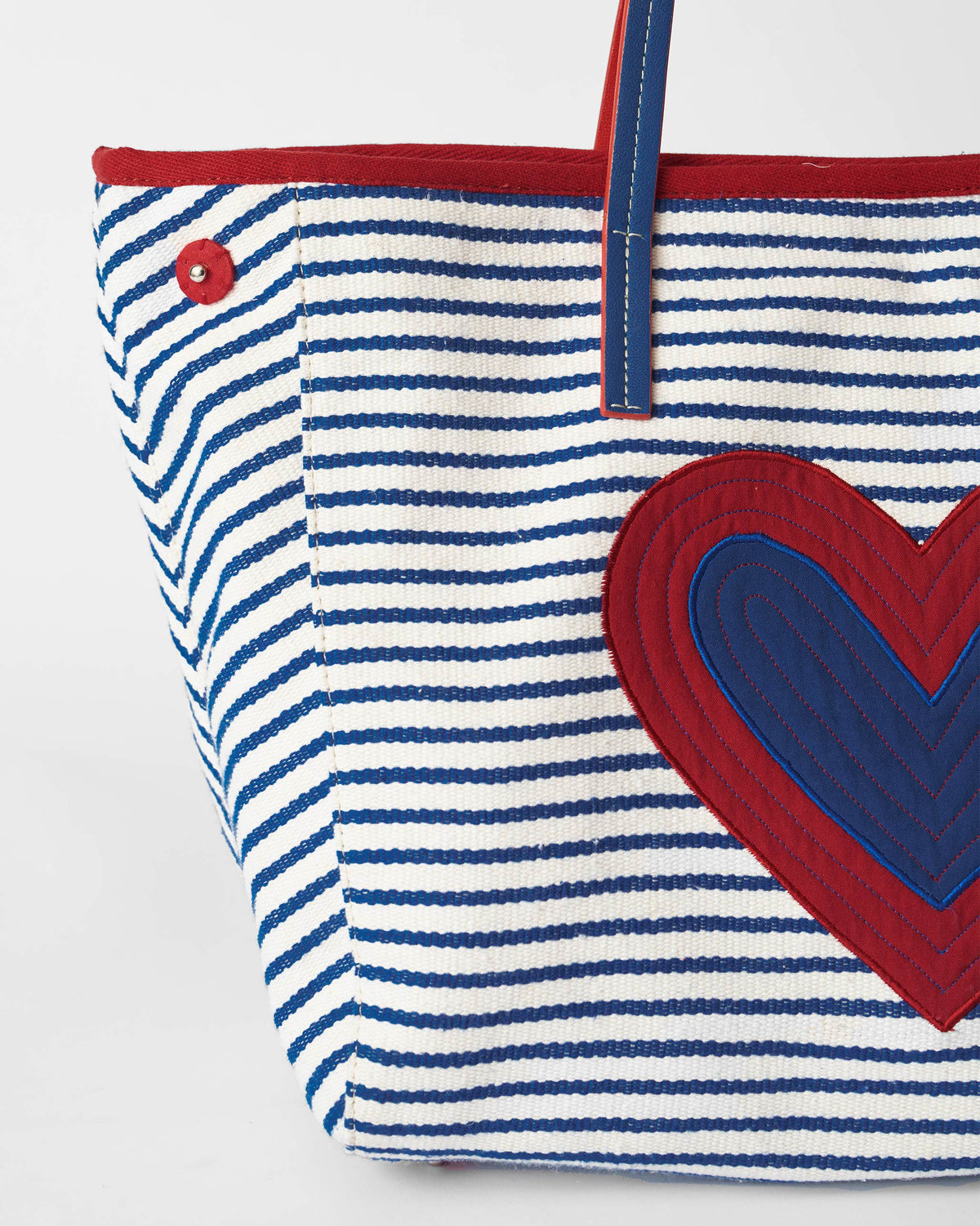 Close-up of the quilted red and blue heart on a striped Kira Bag.