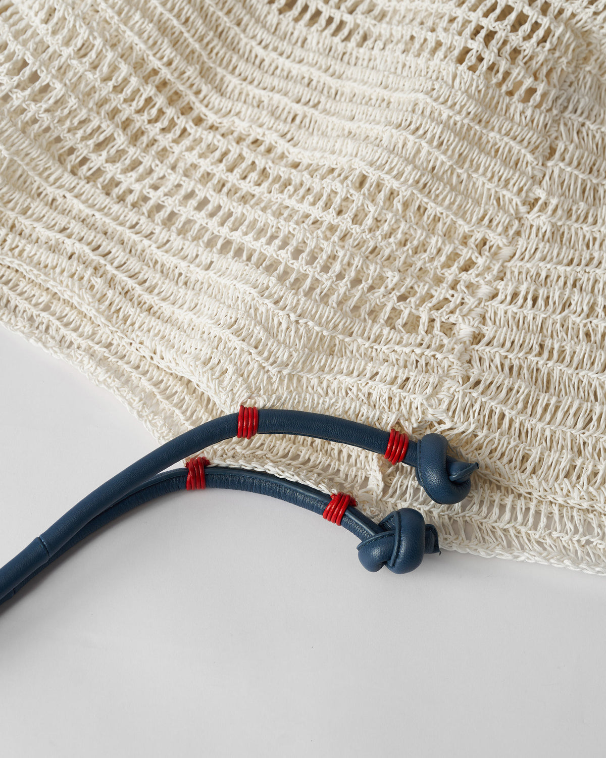 Close-up of navy handle cords with red wraps on cream mesh fabric.