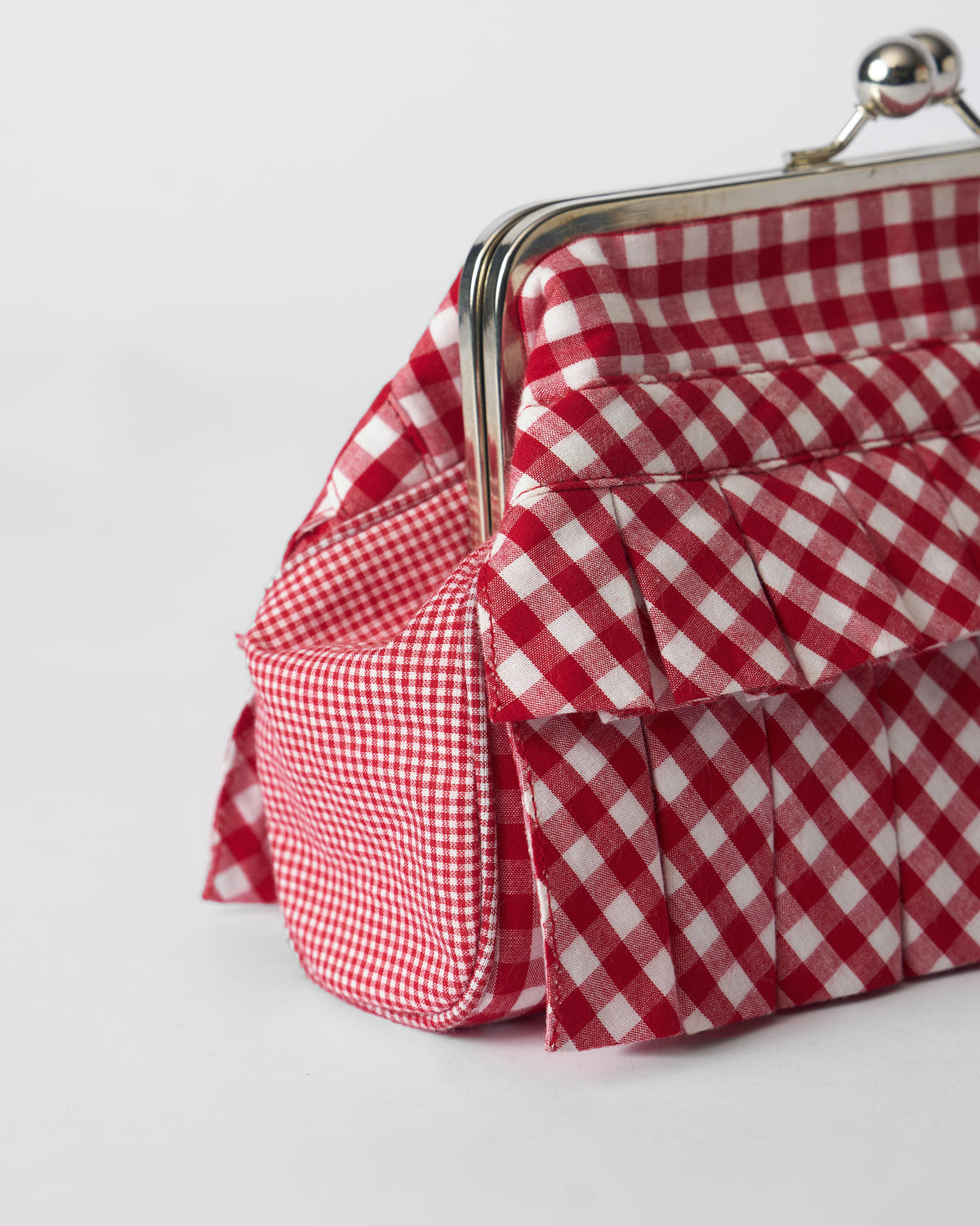 Close-up of the silver kiss-lock on a red and white Pleated Muse Clutch.