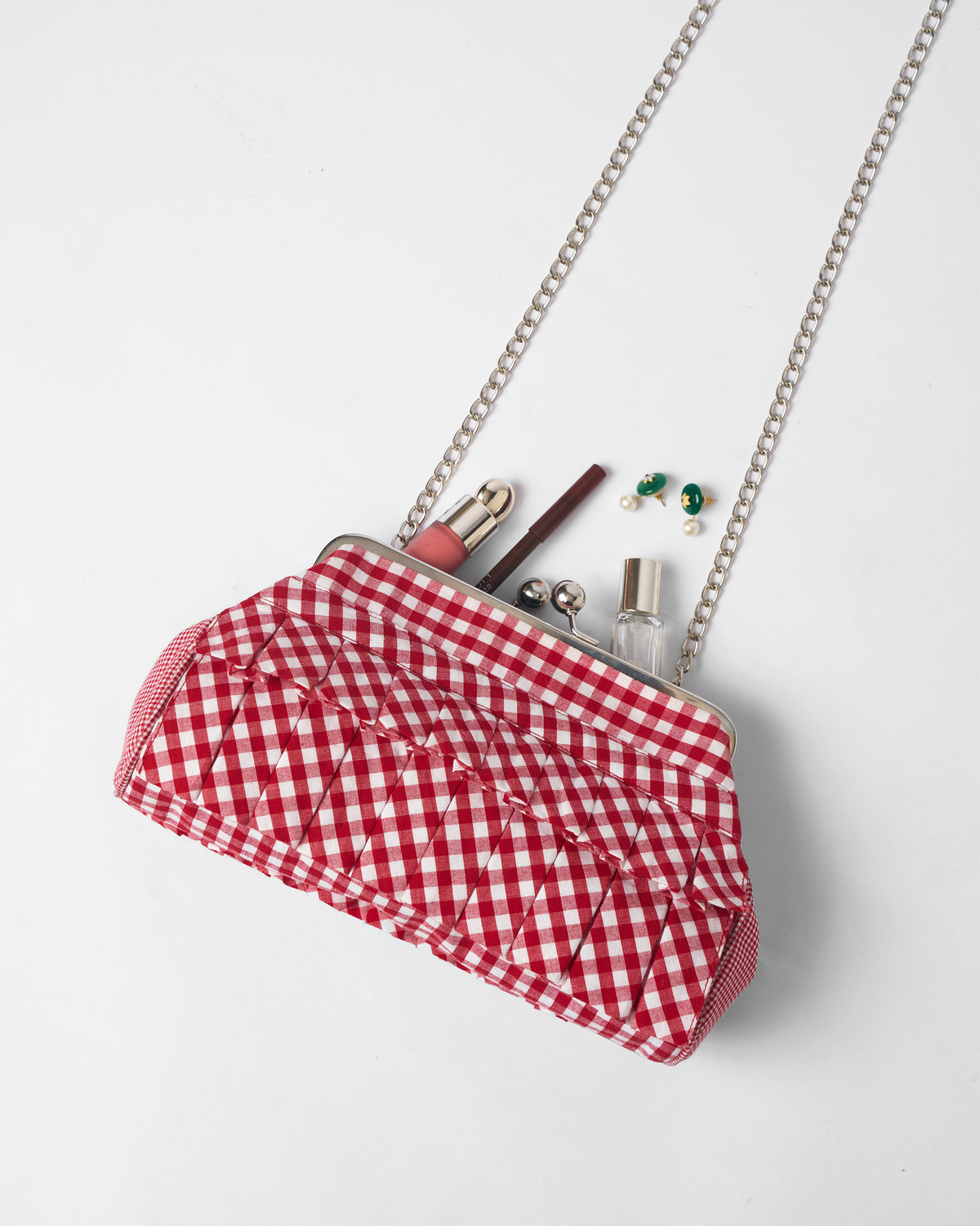 Open red and white Pleated Muse Clutch packed with lipstick and small essentials.
