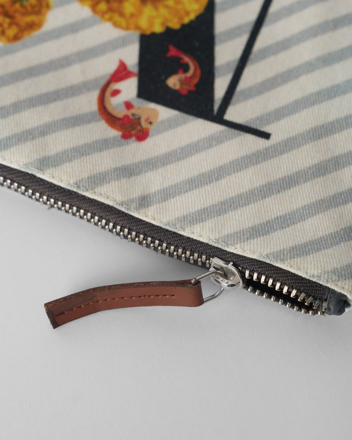 Close-up of the brown leather zipper pull on an ivory Machli Pouch.