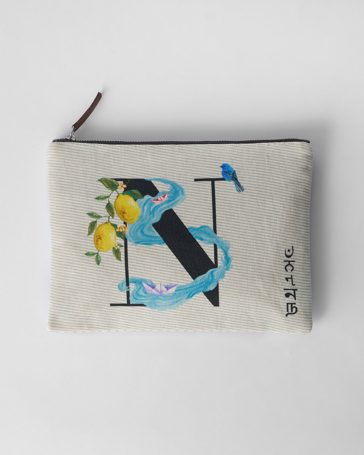 Ivory Nilambari Pouch with a black N print, lemons, and blue paper boats.