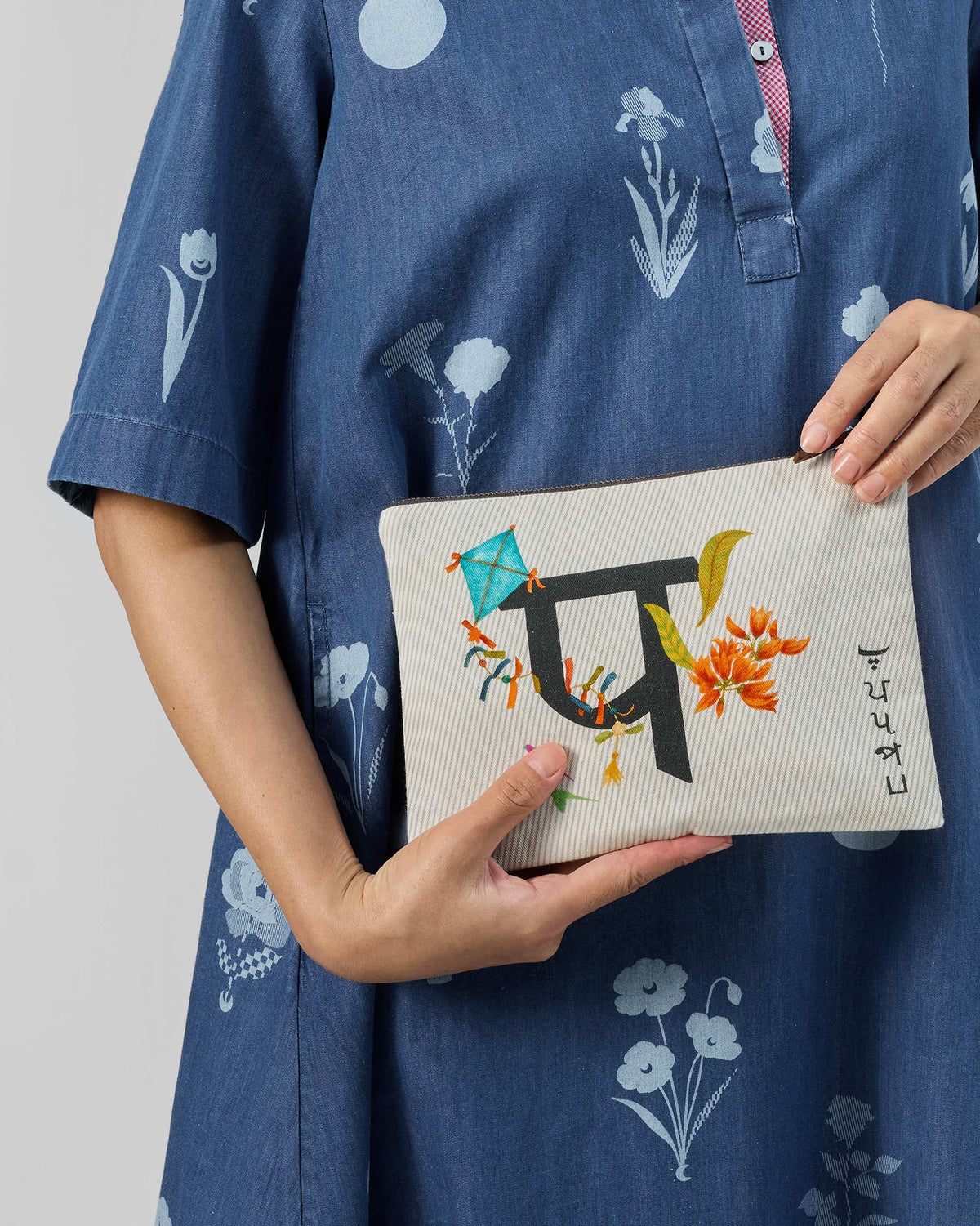 Ivory Palash Pouch with a black letter print, blue kite, and orange flowers.