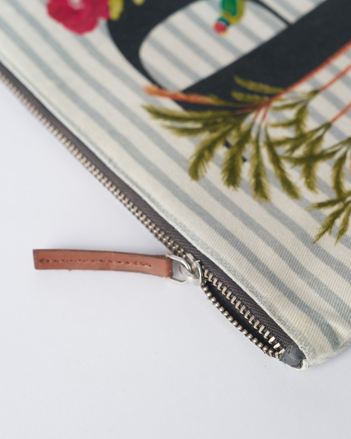 Close-up of the brown leather zipper pull on an ivory Palash Pouch.