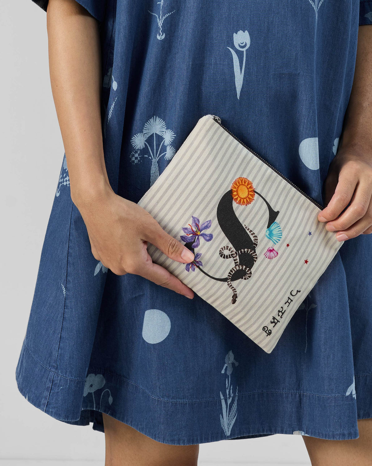Person holding an ivory Sitara Pouch with a black letter S and flower motifs.