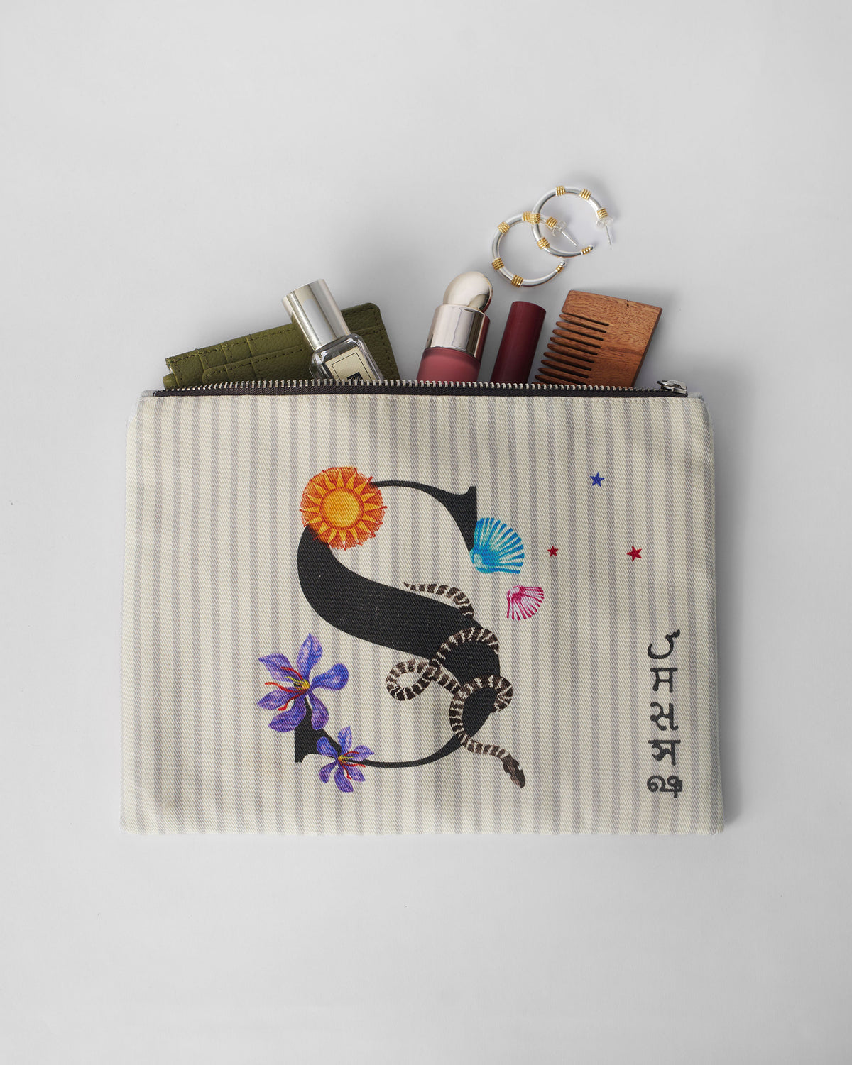 Open ivory Sitara Pouch with a letter S graphic and small essentials inside.