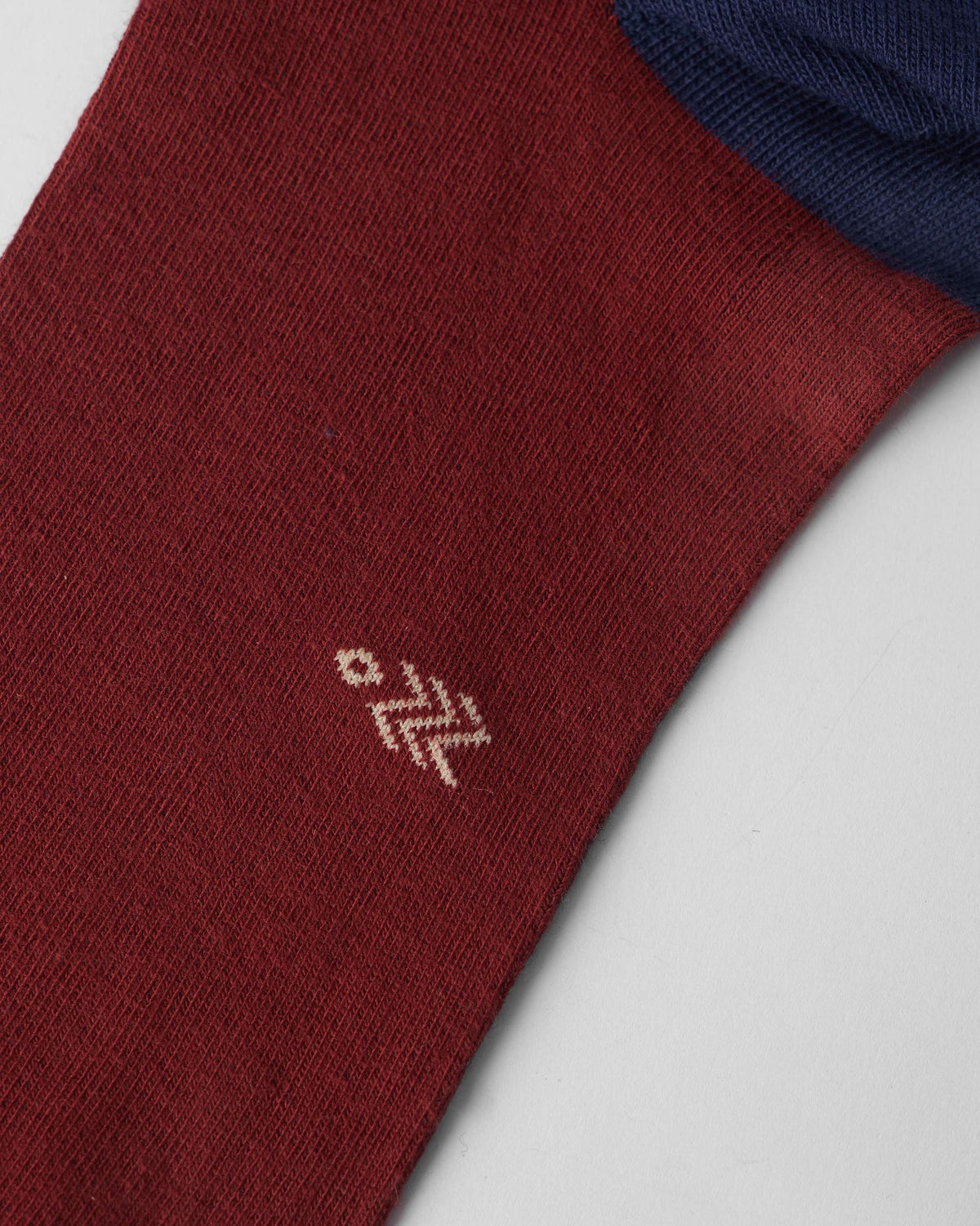 Close-up of a maroon sock showing the beige Nicobar logo near the foot.