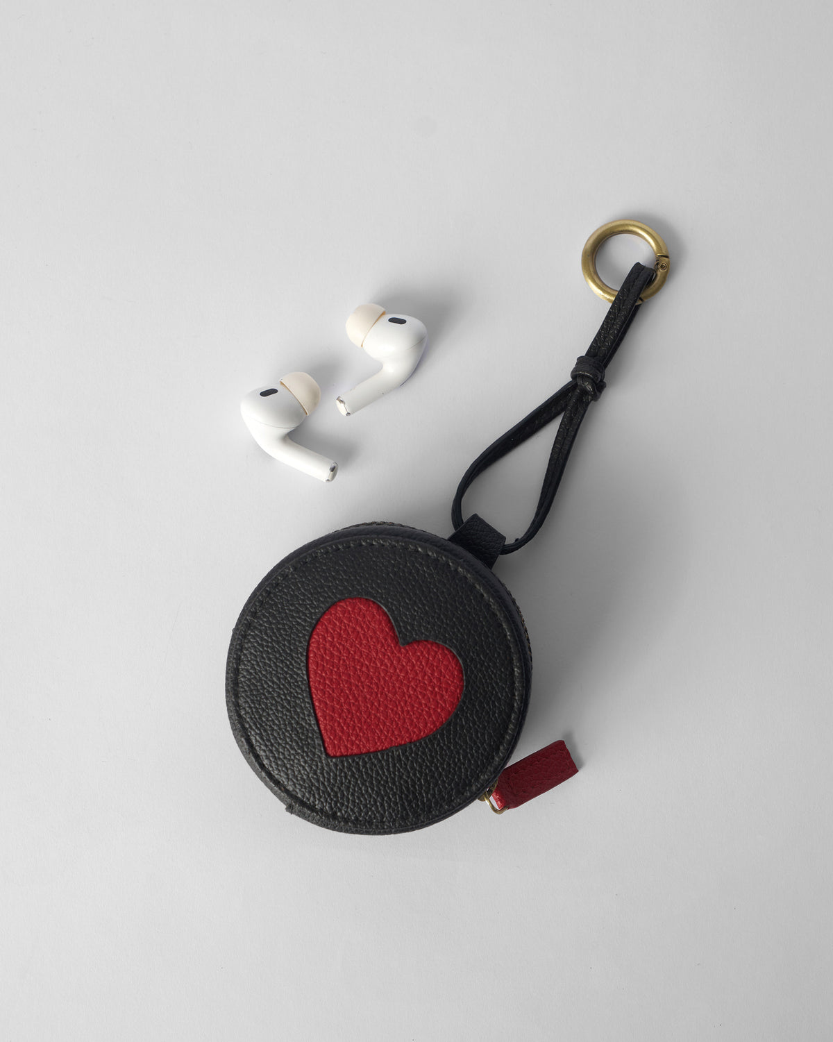 Black Nova Charm with a red heart next to wireless earbuds for scale.