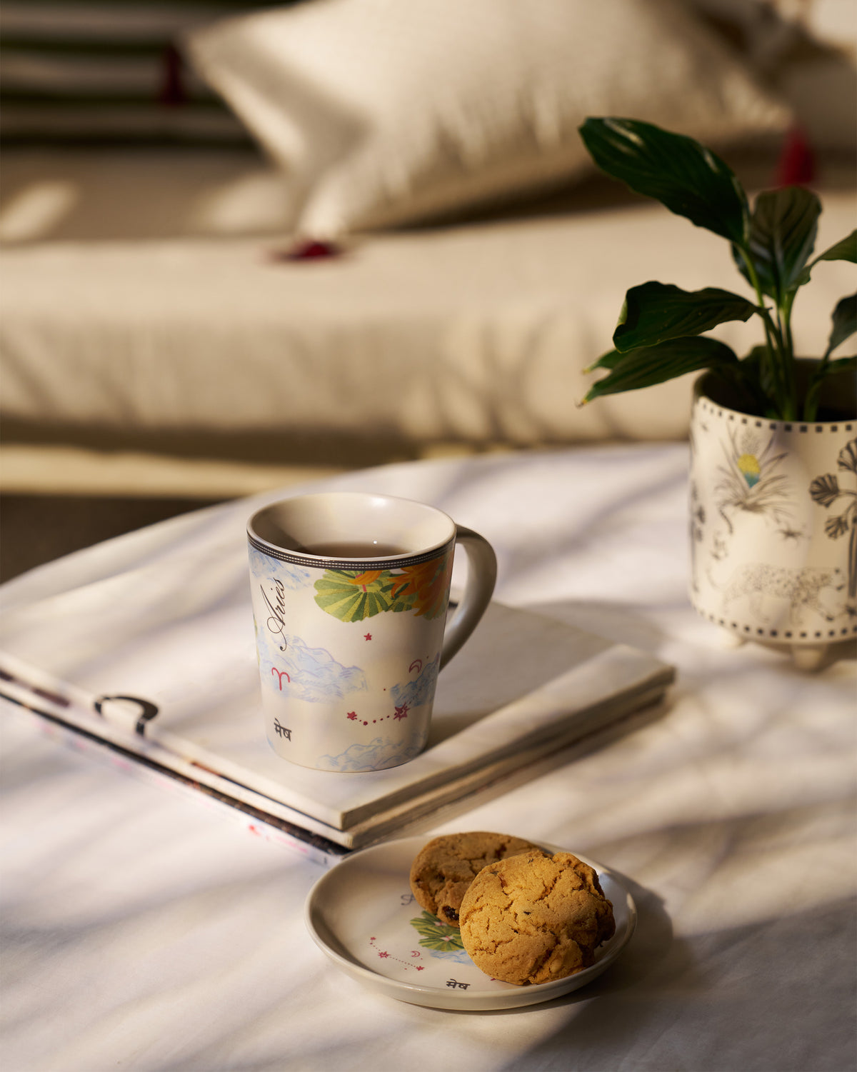 Nico Aries mug and tea plate with cookies in a sunlit setting.