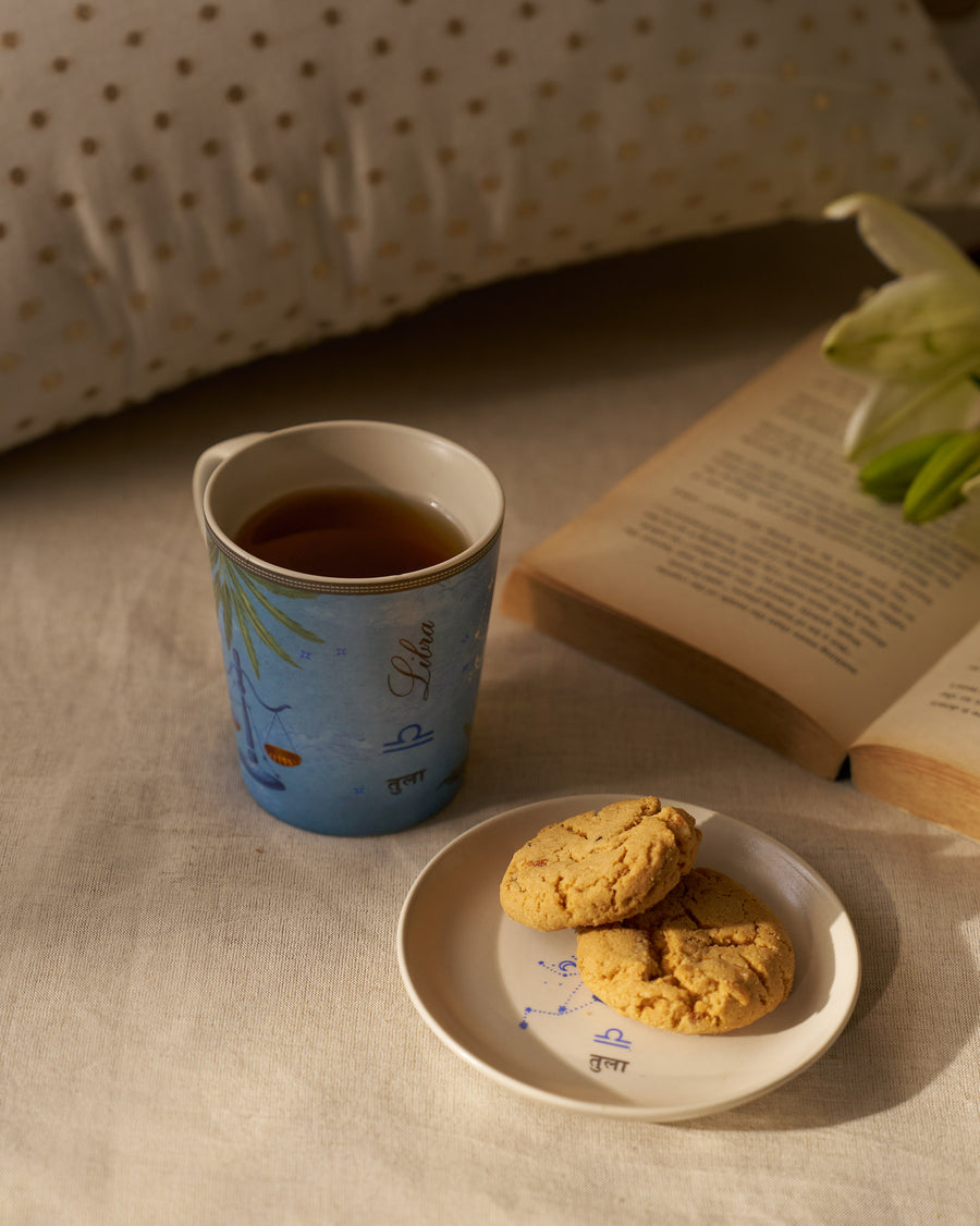 The Libra mug of tea beside cookies and an open book