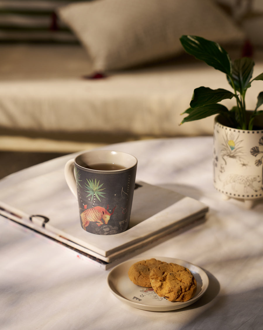 The Taurus mug on a book beside a plate of cookies