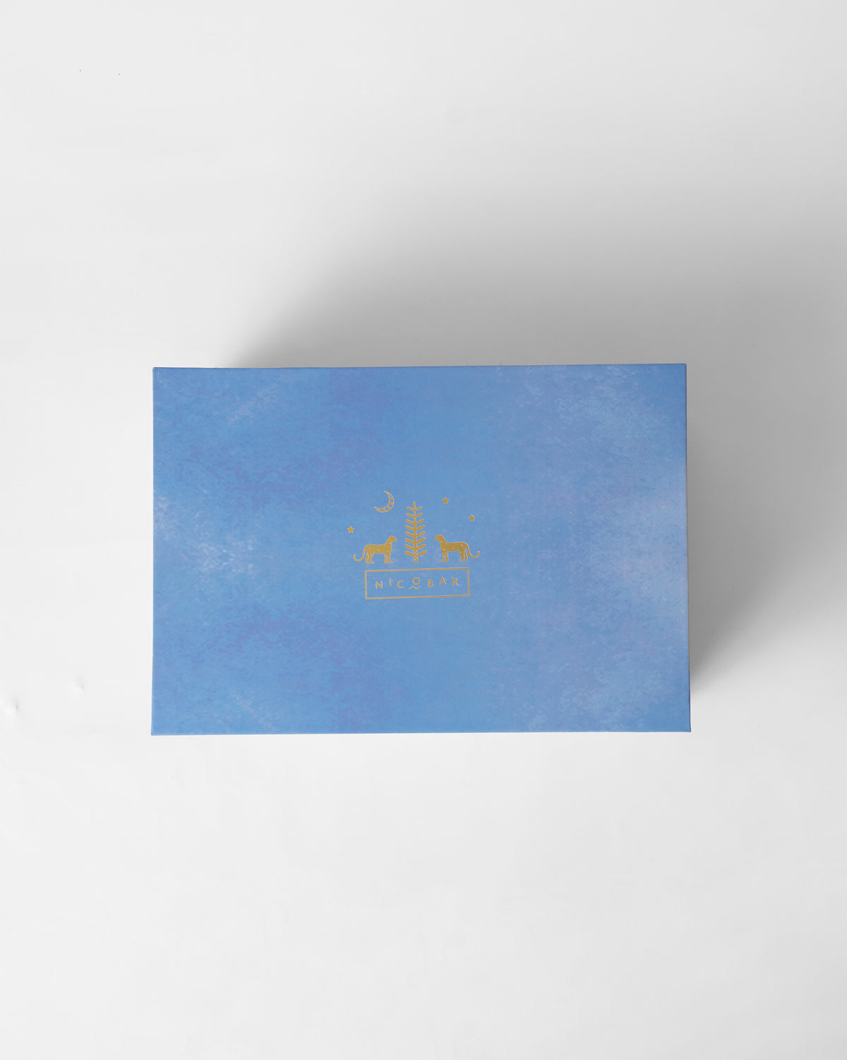 Blue Nicobar gift box lid with a gold logo.