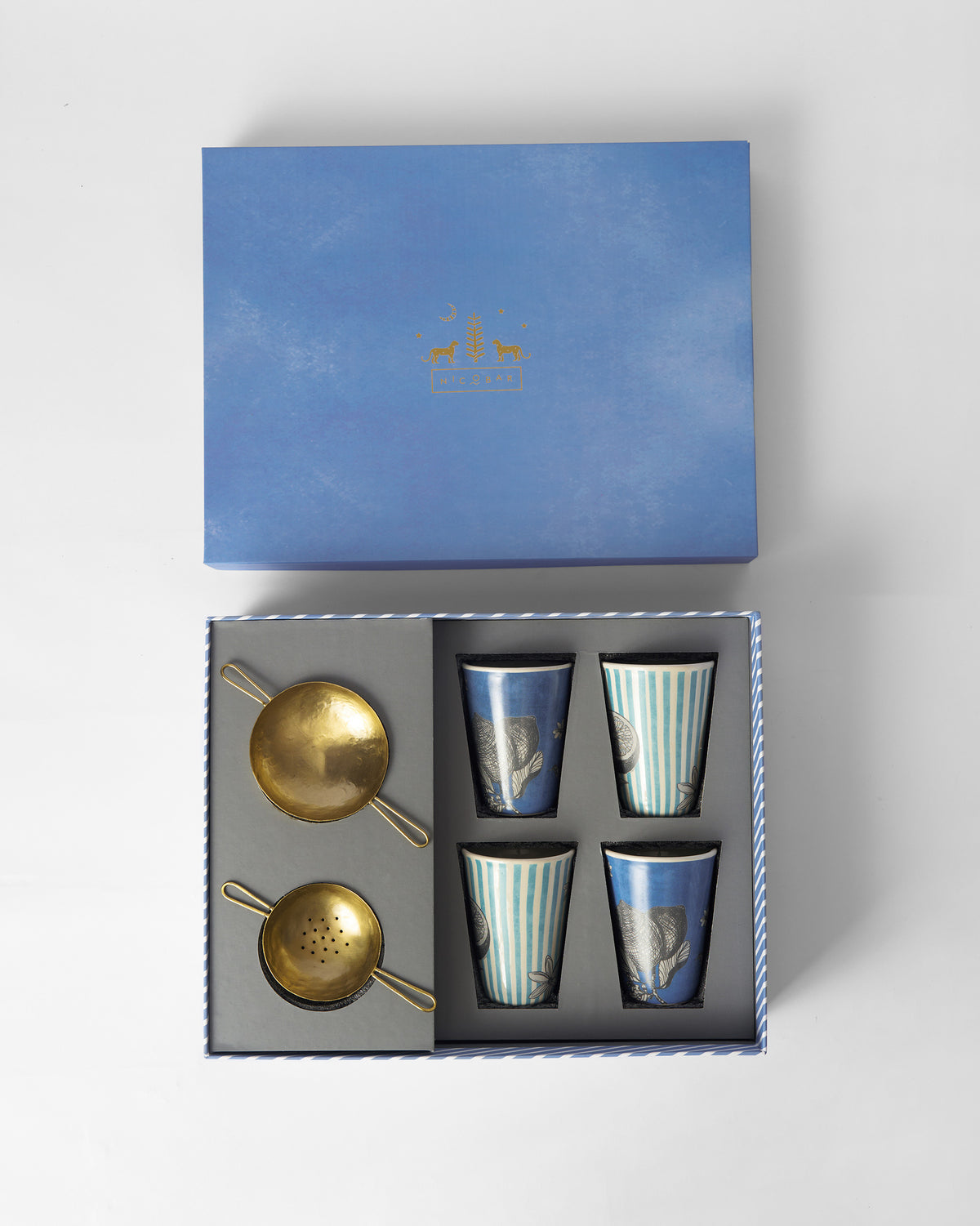 Open Neel gift box holding four blue kulhars and two brass chai strainers.