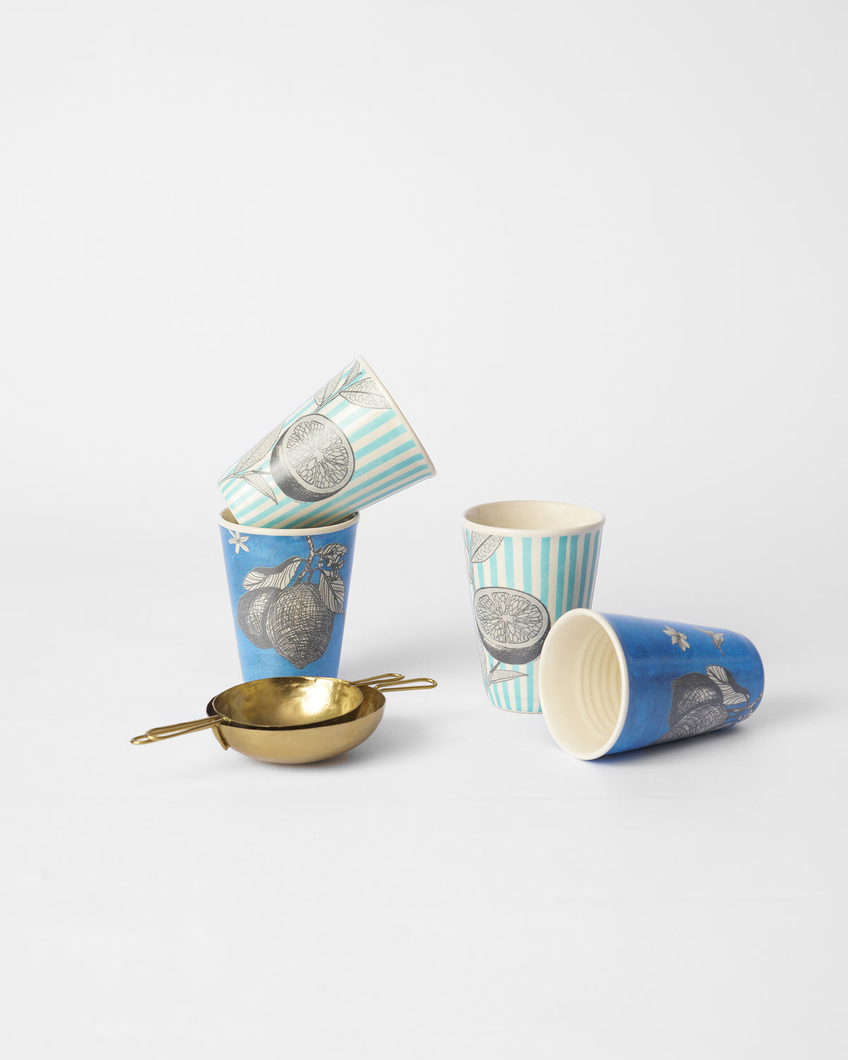 Four Neel kulhars in striped and solid blue citrus prints with brass chai strainers.