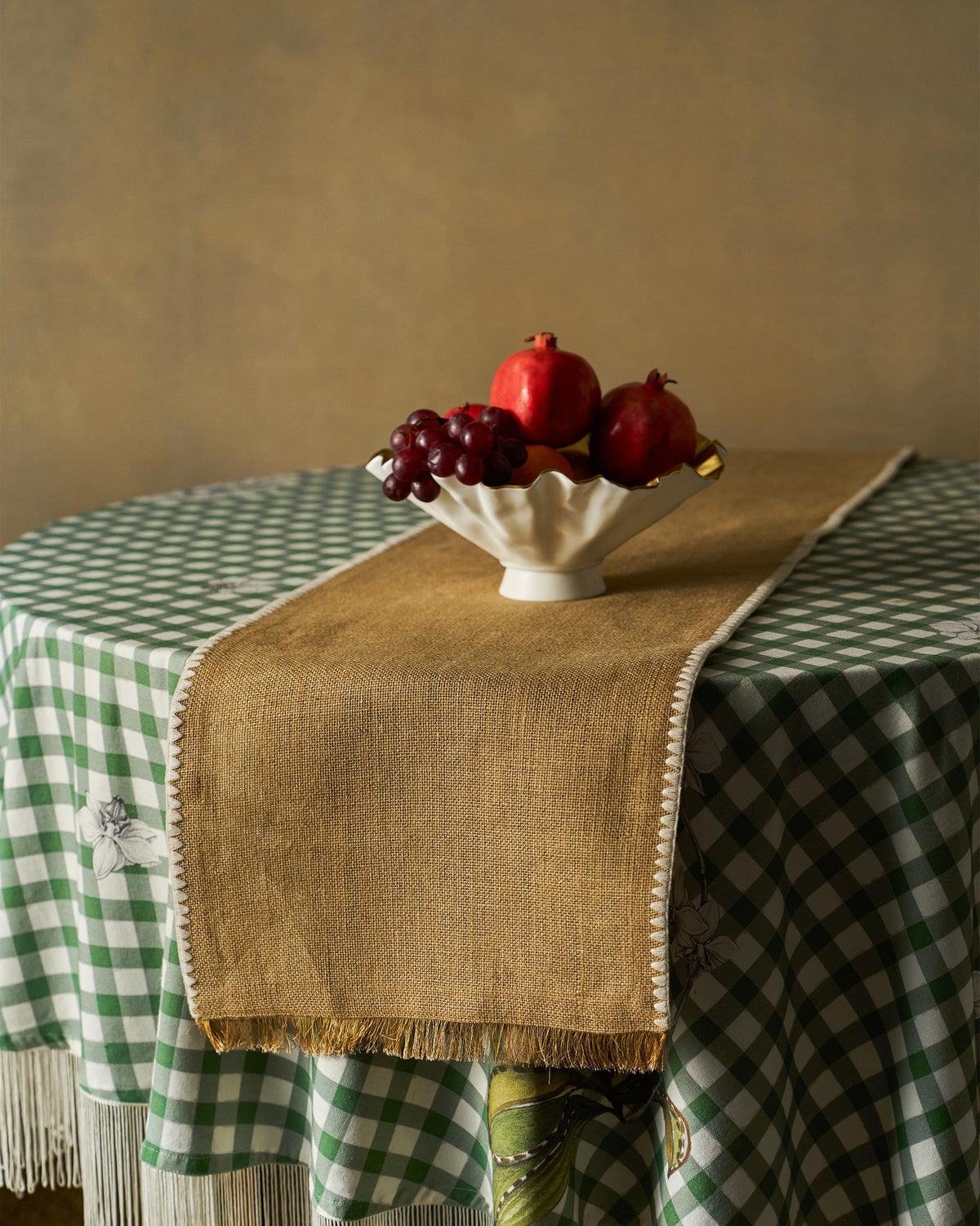 Kaveri Runner in tan with fringed ends, laid across a green gingham tablecloth.