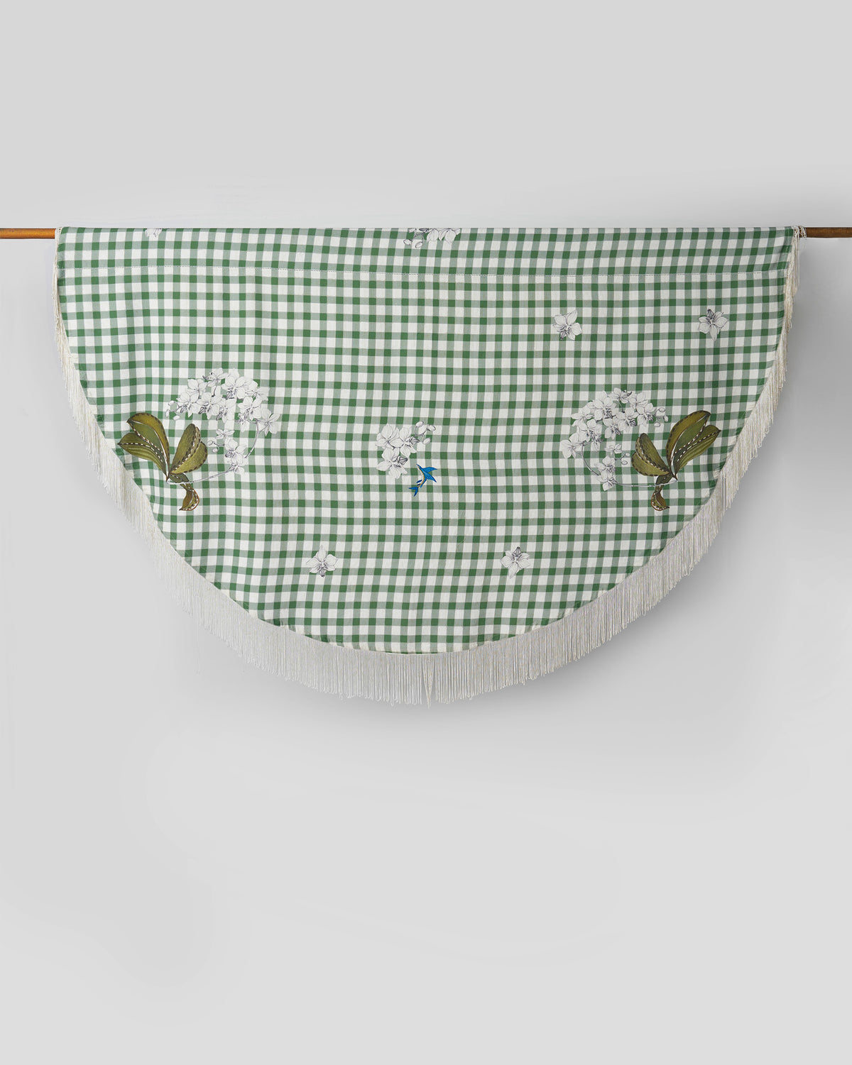 Kaveri Table Cover in green gingham with white fringe, hung over a rod.