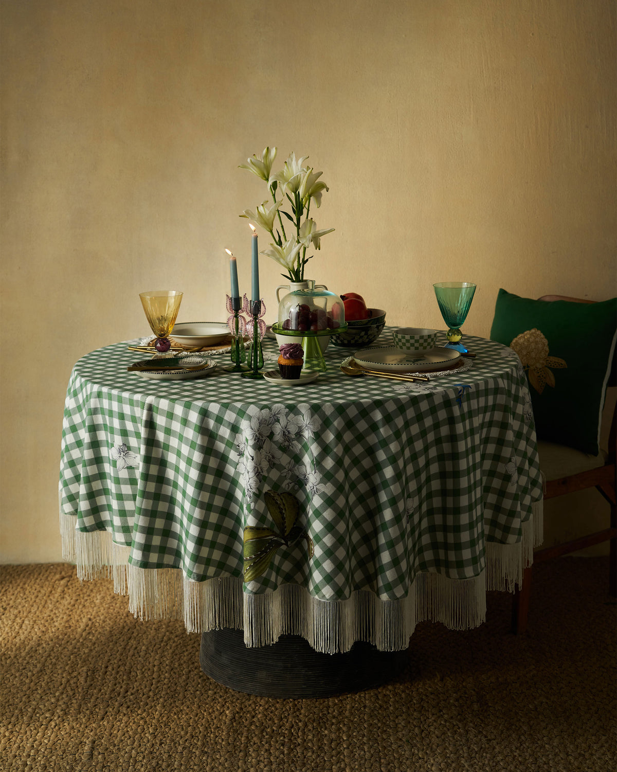 Kaveri Table Cover in green gingham with white fringe, laid on a round table.
