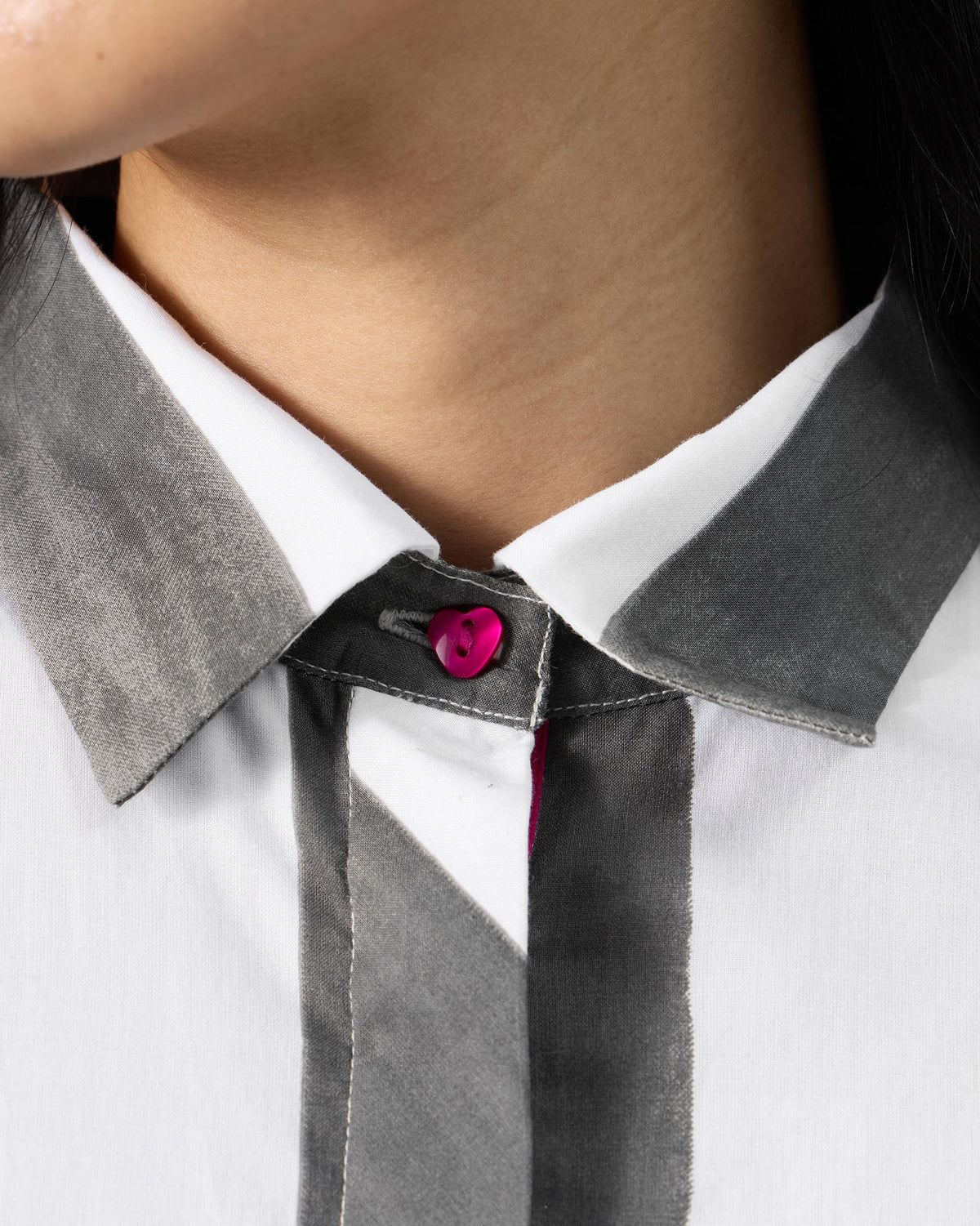 Close-up of a fuchsia heart button on a charcoal striped Kuro Dress collar.