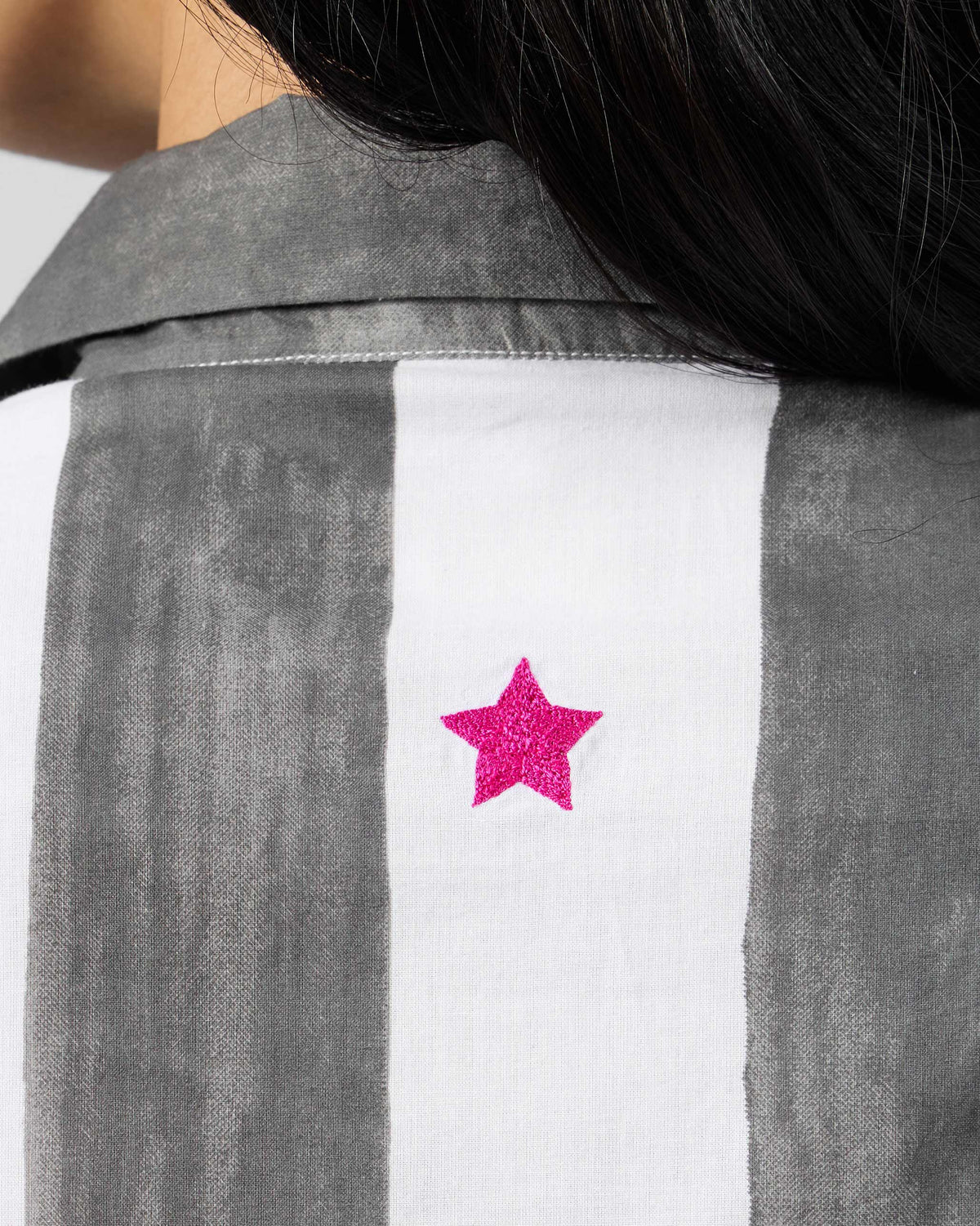 Close-up of a pink embroidered star on a charcoal striped Kuro Dress.