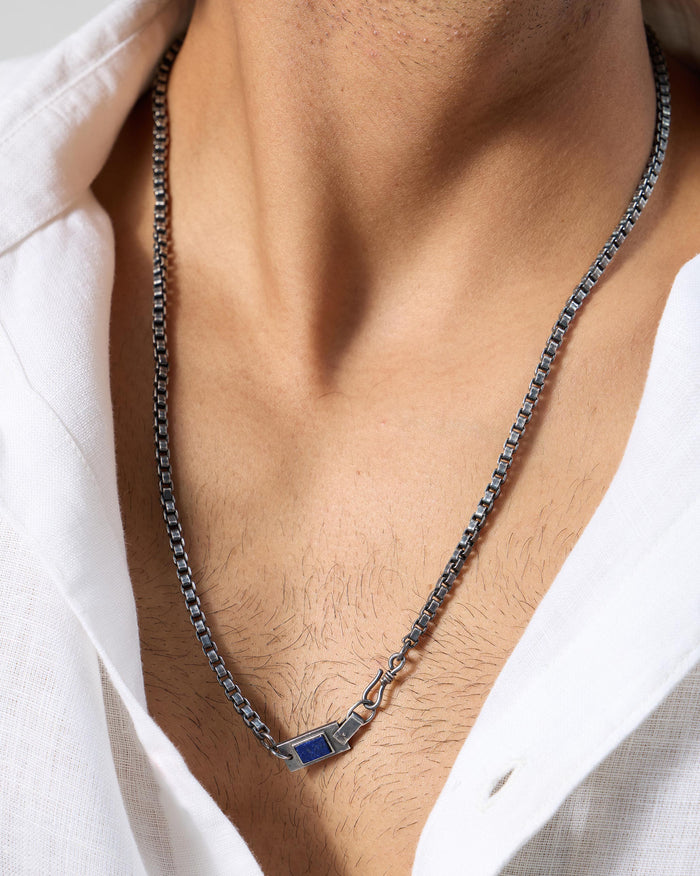 Silver Taro chain with a rectangular lapis accent worn at an open collar.