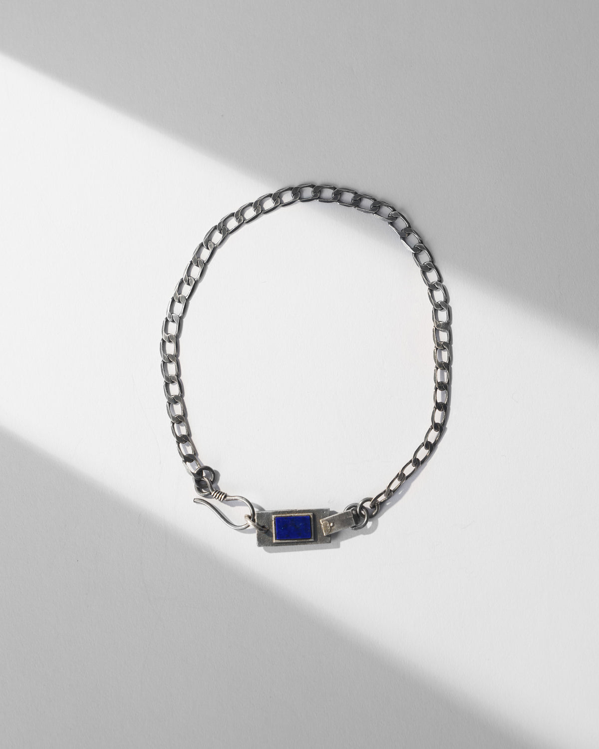 Silver Taro bracelet with curb links and a blue stone plaque laid flat.