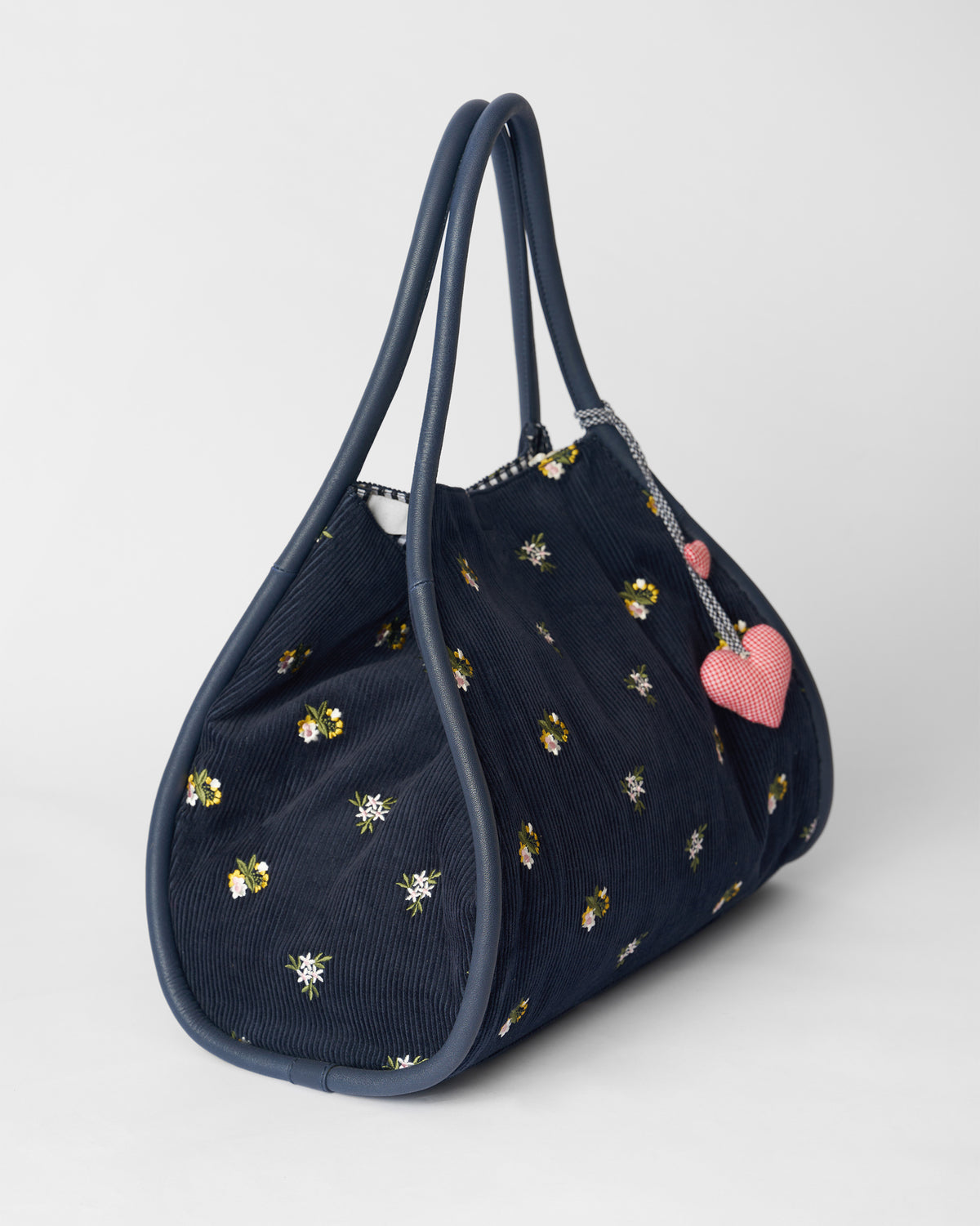 Three-quarter view of a navy Ditsy bag with floral embroidery and heart charms.
