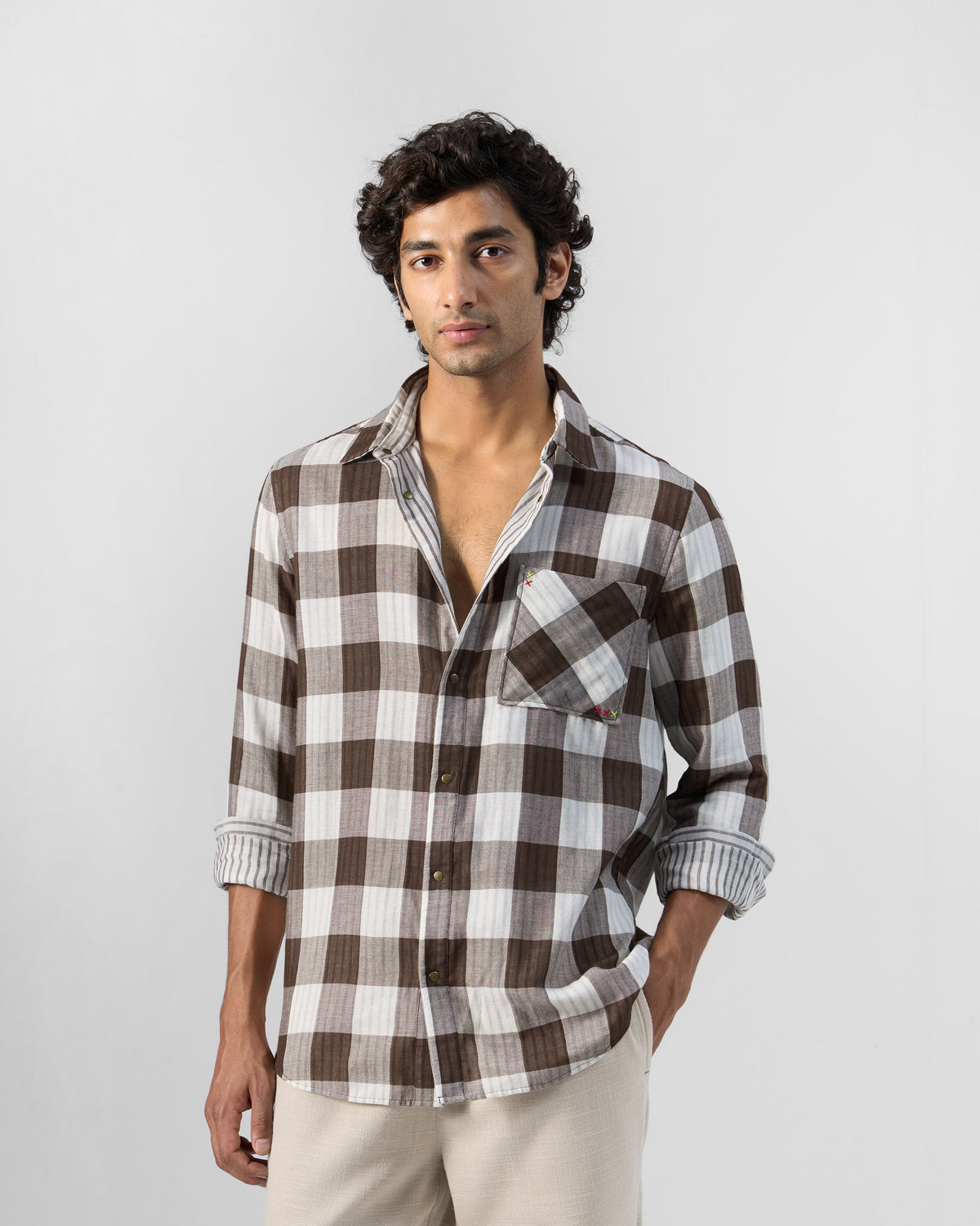 Person wearing a brown check Milaan shirt with rolled sleeves.