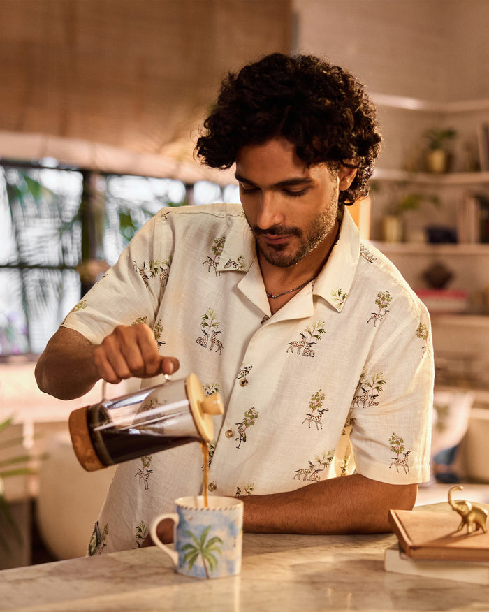 Person wearing a cream Bena shirt with a deer and tree print.