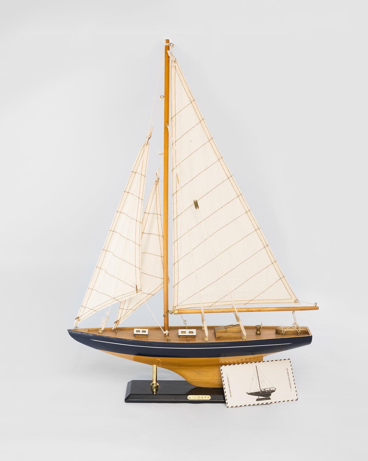 Large Sail Boat Home Accent, a wooden model with cream sails and a navy hull, with a postcard beside it.
