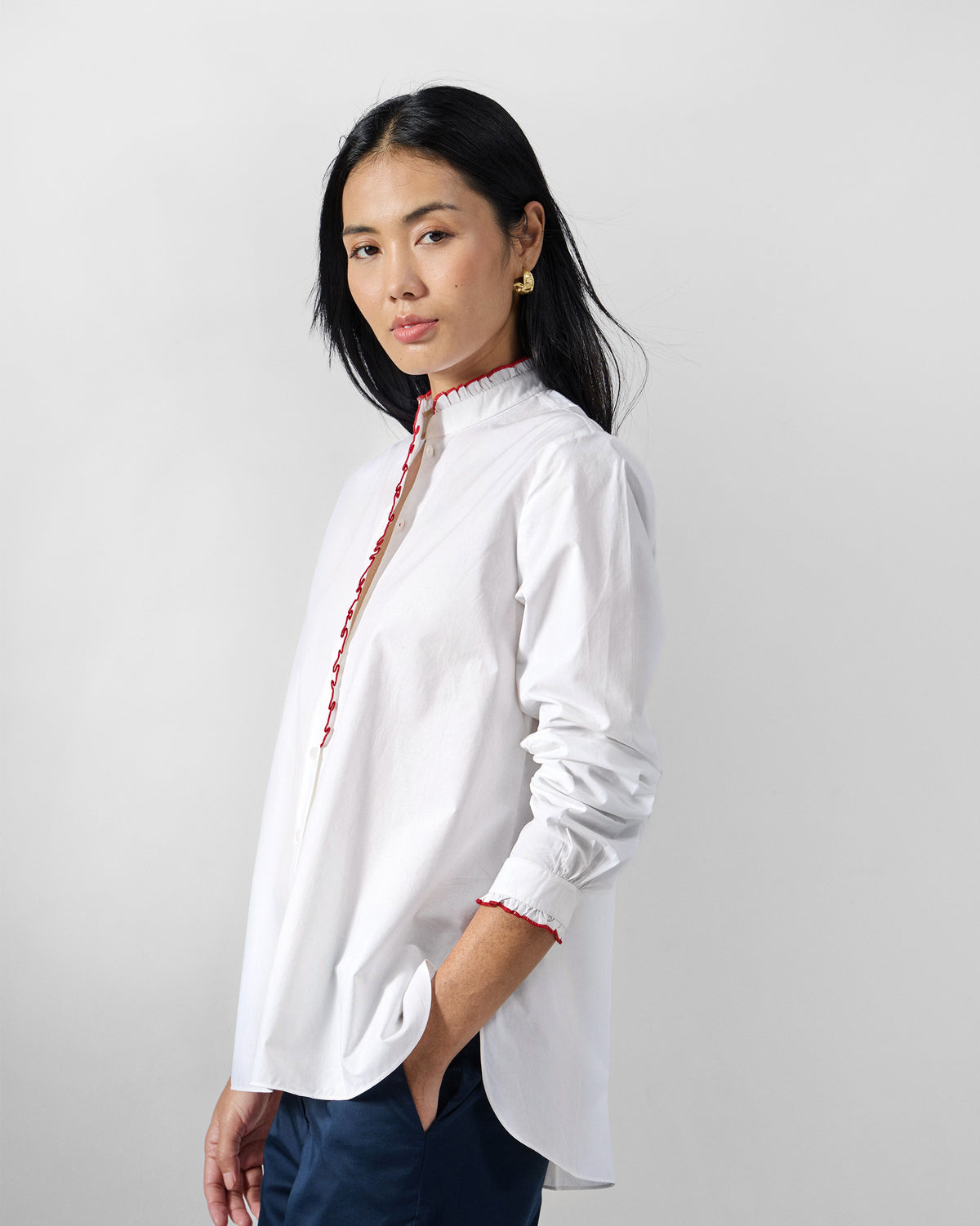 Side view of a white Sora ruffle shirt with red trim.