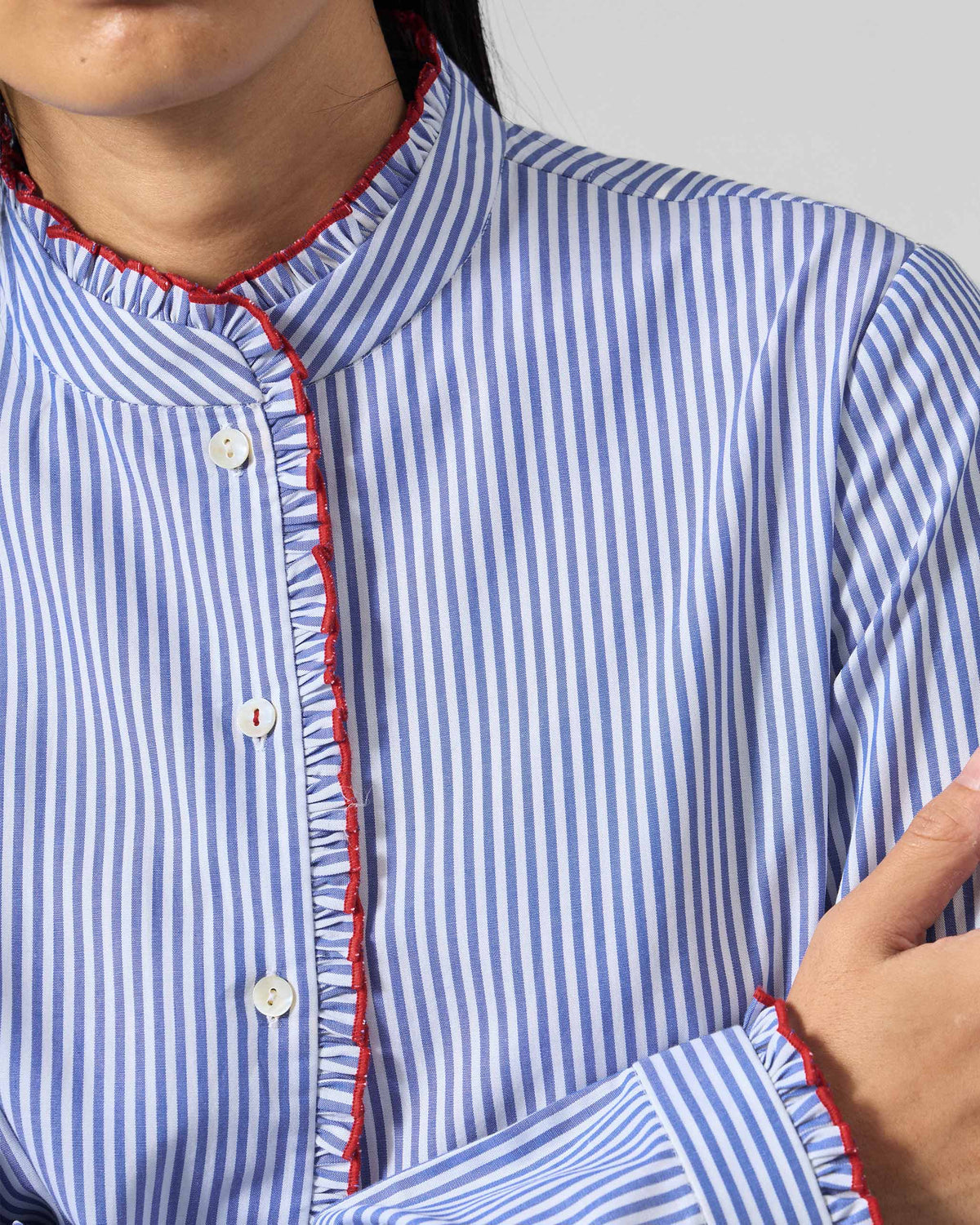 Close-up of a blue and white striped Sora ruffle shirt showing red ruffle trim.