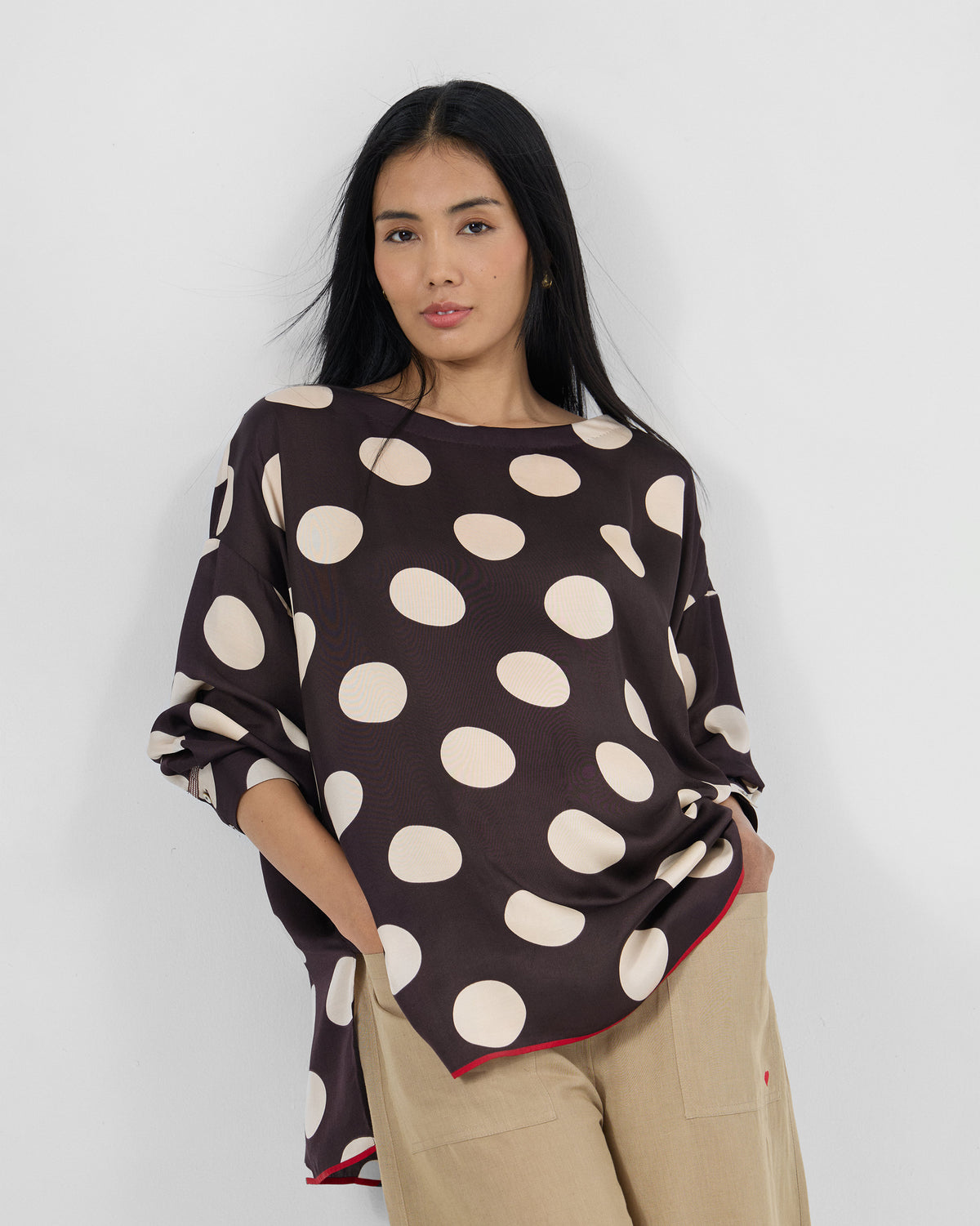 Person wearing a brown Yava Top with ivory polka dots and a red piped hem.