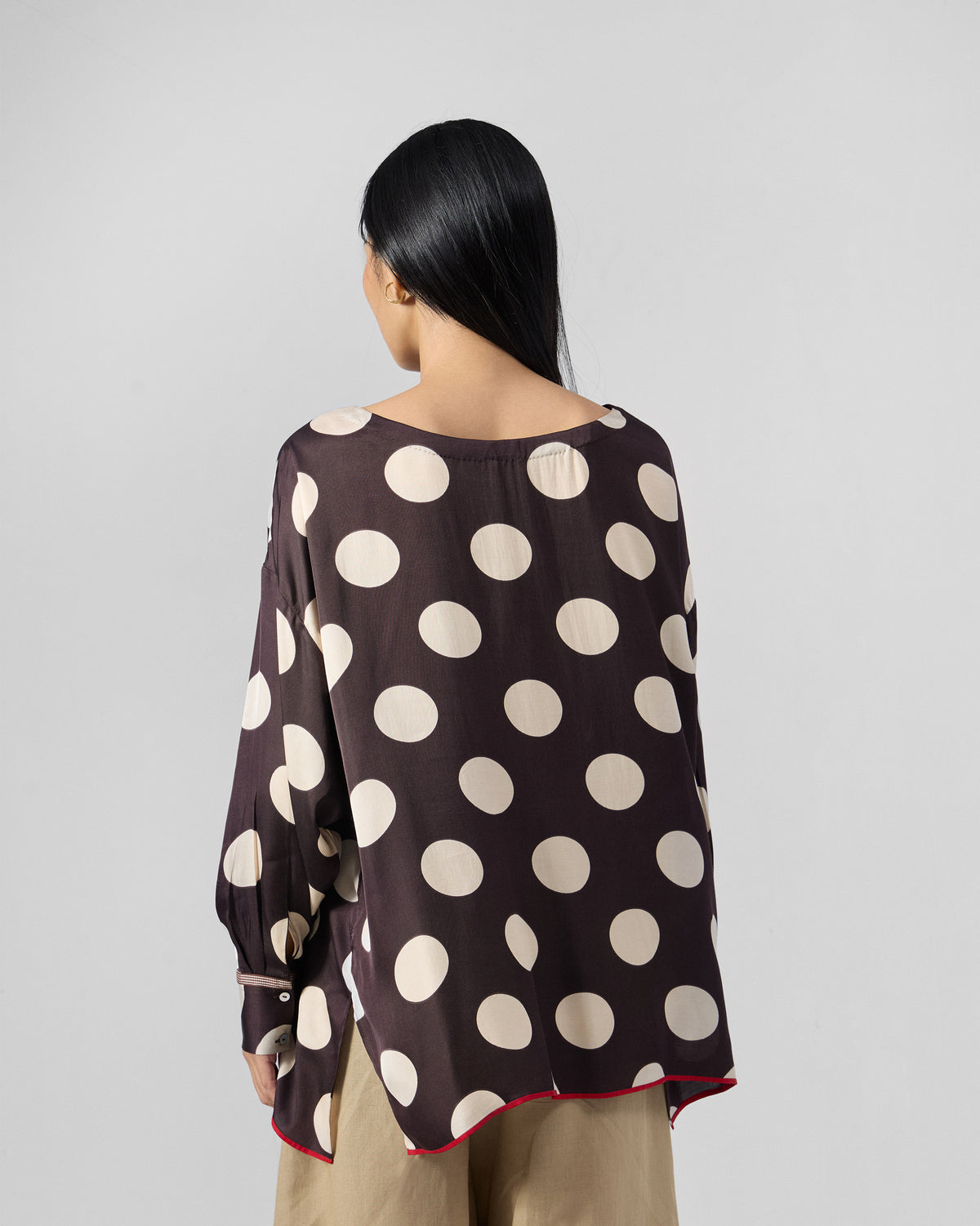 Back of a brown Yava Top with ivory polka dots and a red piped hem.