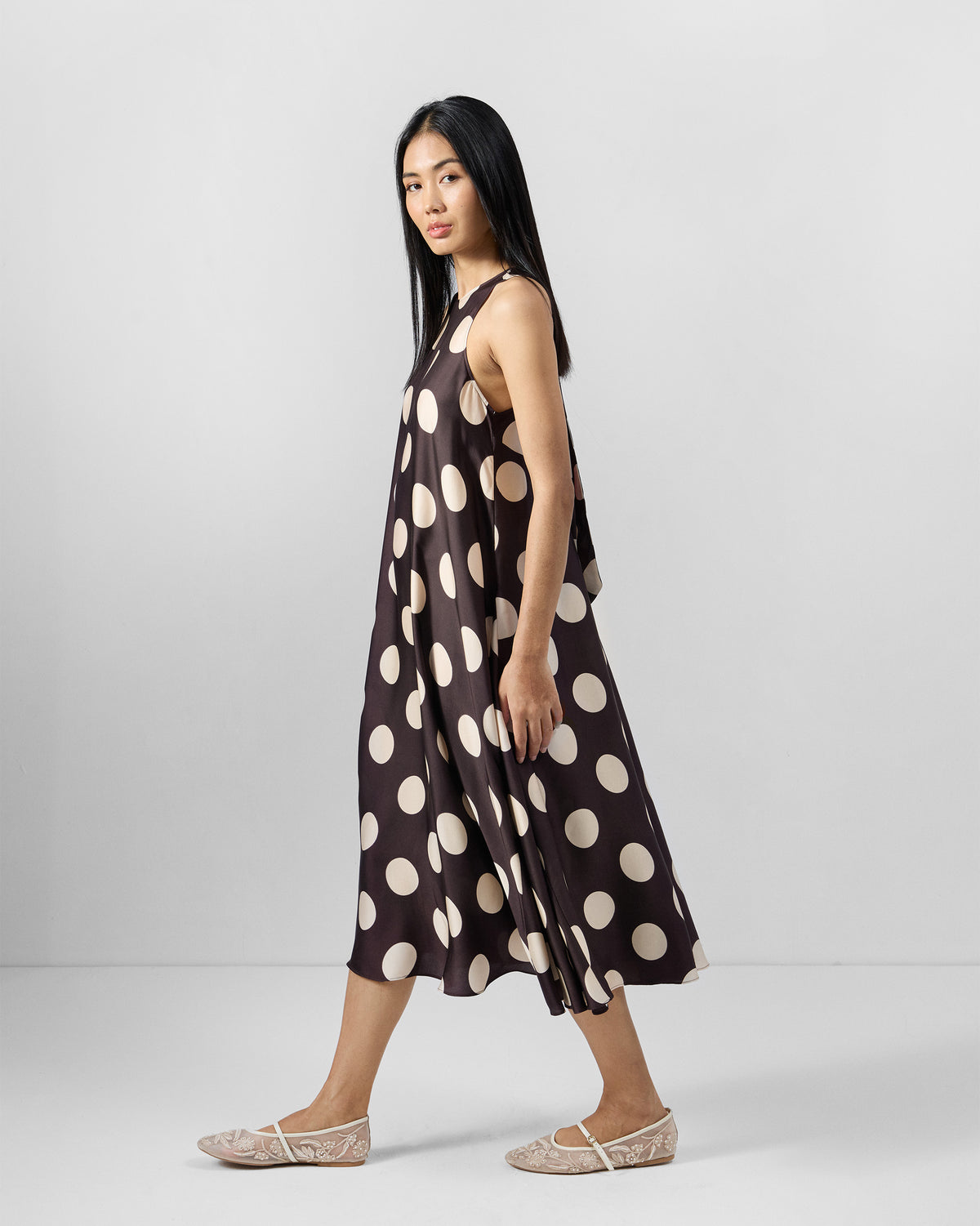 Side view of a brown Kinaar Dress with ivory polka dots and a flared midi hem.