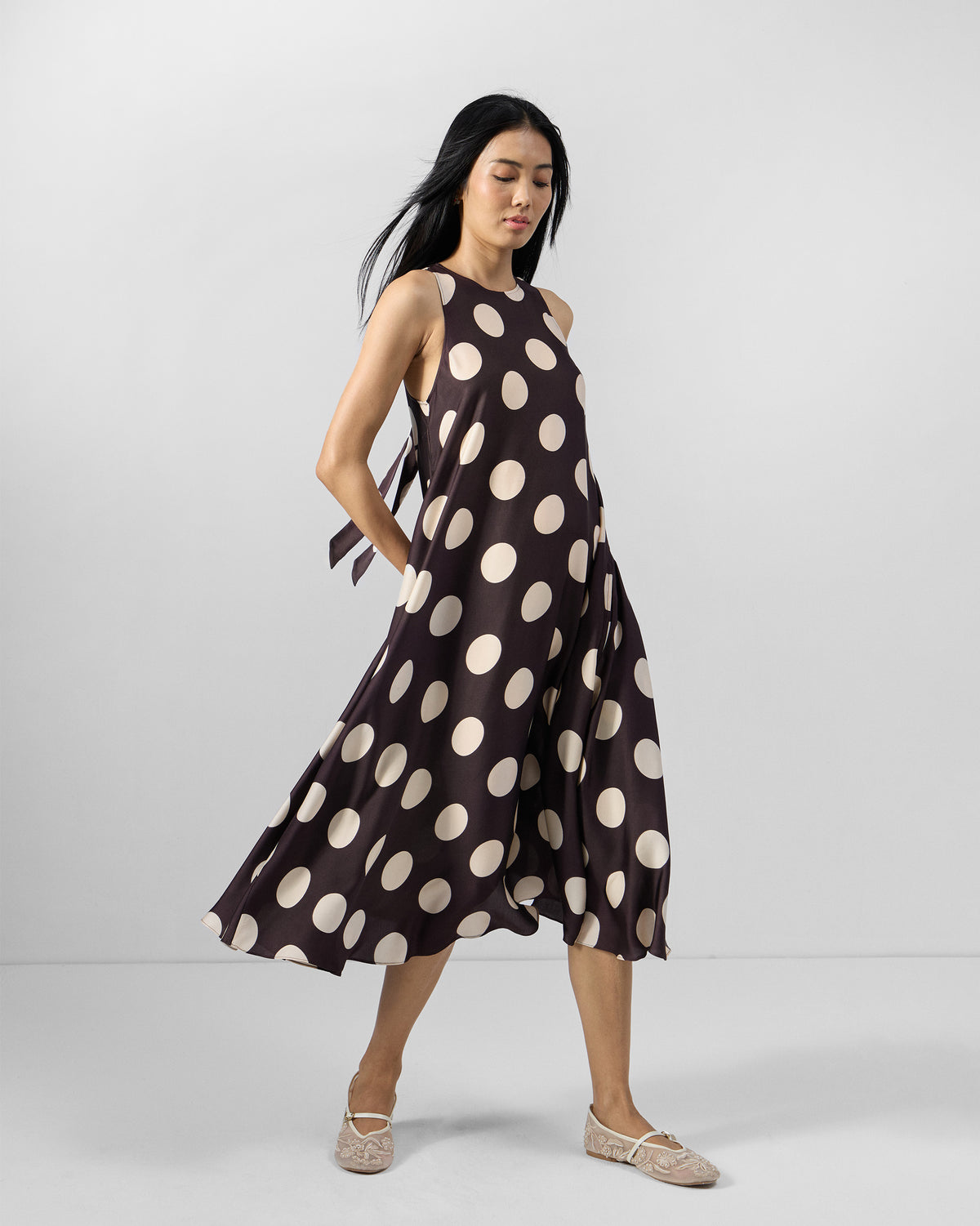 Person wearing a brown Kinaar Dress with ivory polka dots and a sleeveless midi fit.