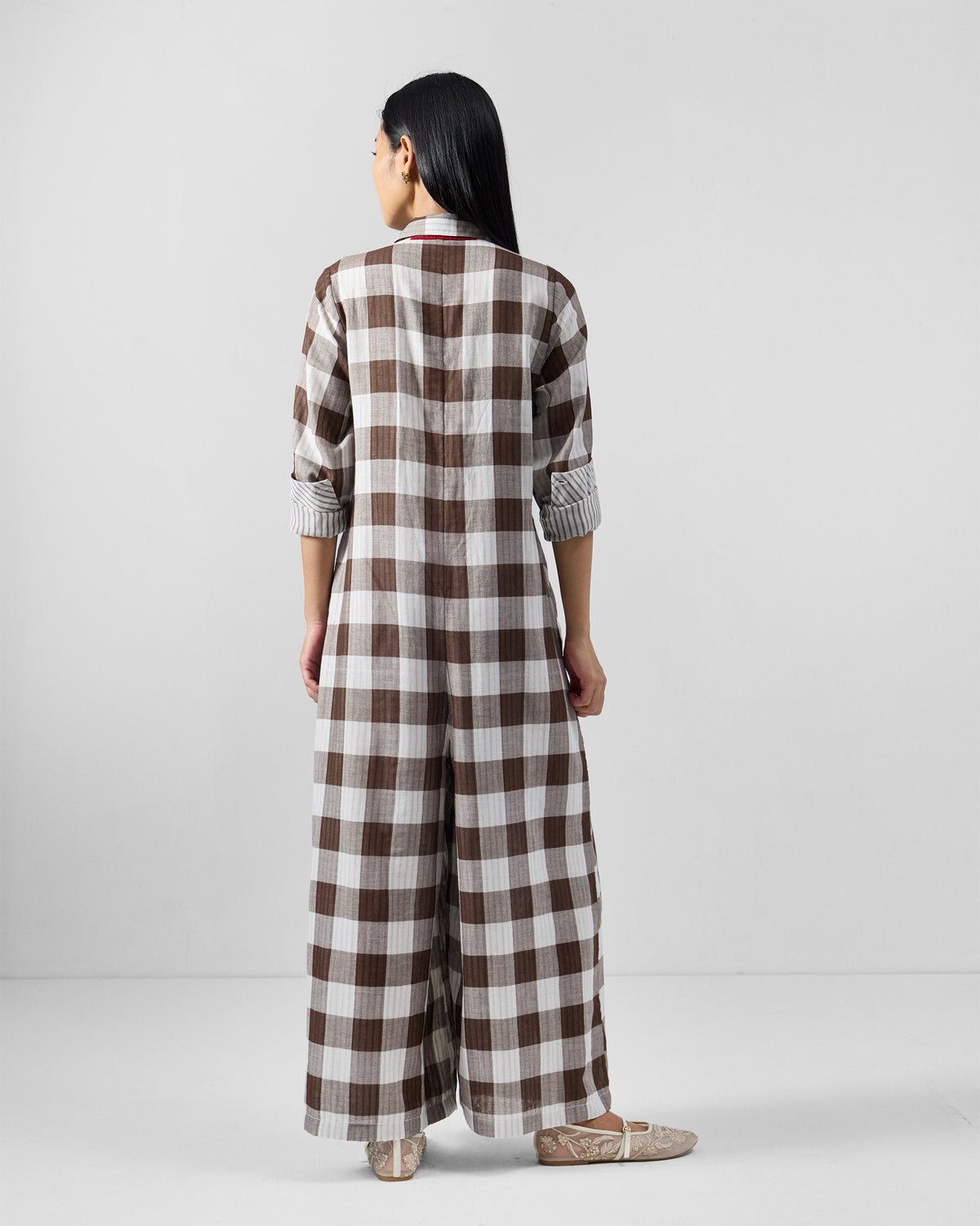 Back of a brown and ivory check jumpsuit with red piping along the collar.