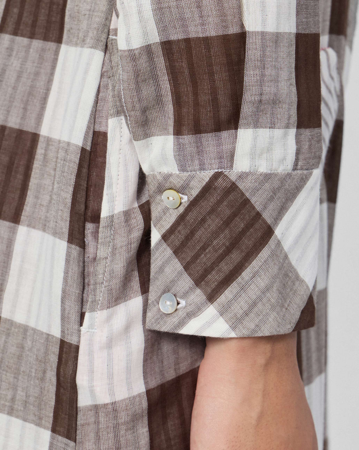 Close-up of a bias-cut check cuff with pearl buttons on the cotton jumpsuit.