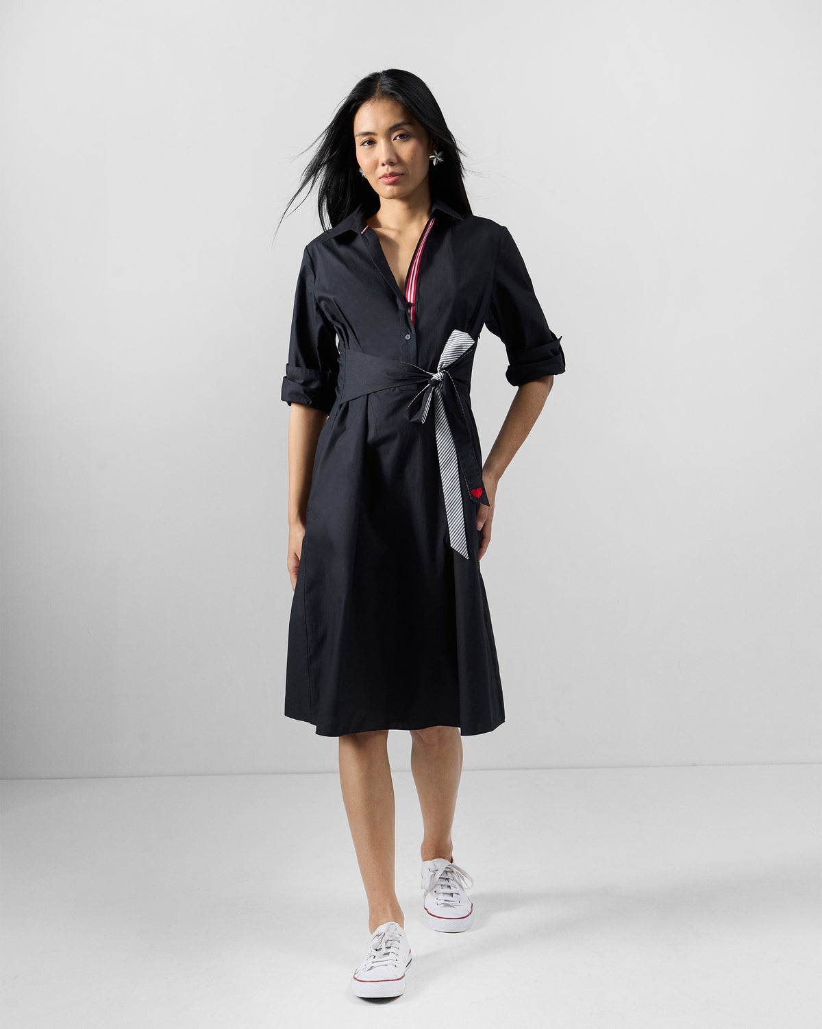Person wearing a black knee-length shirt dress with a waist tie.