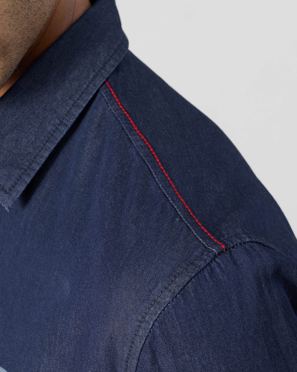 Close-up of red topstitching on an indigo denim Classic shirt shoulder.