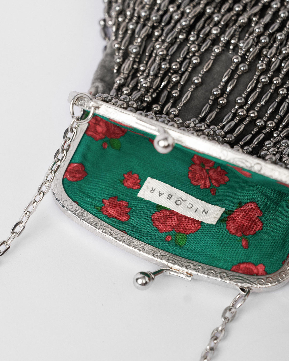 Open silver beaded clutch showing green rosebud lining and kiss-lock clasp.