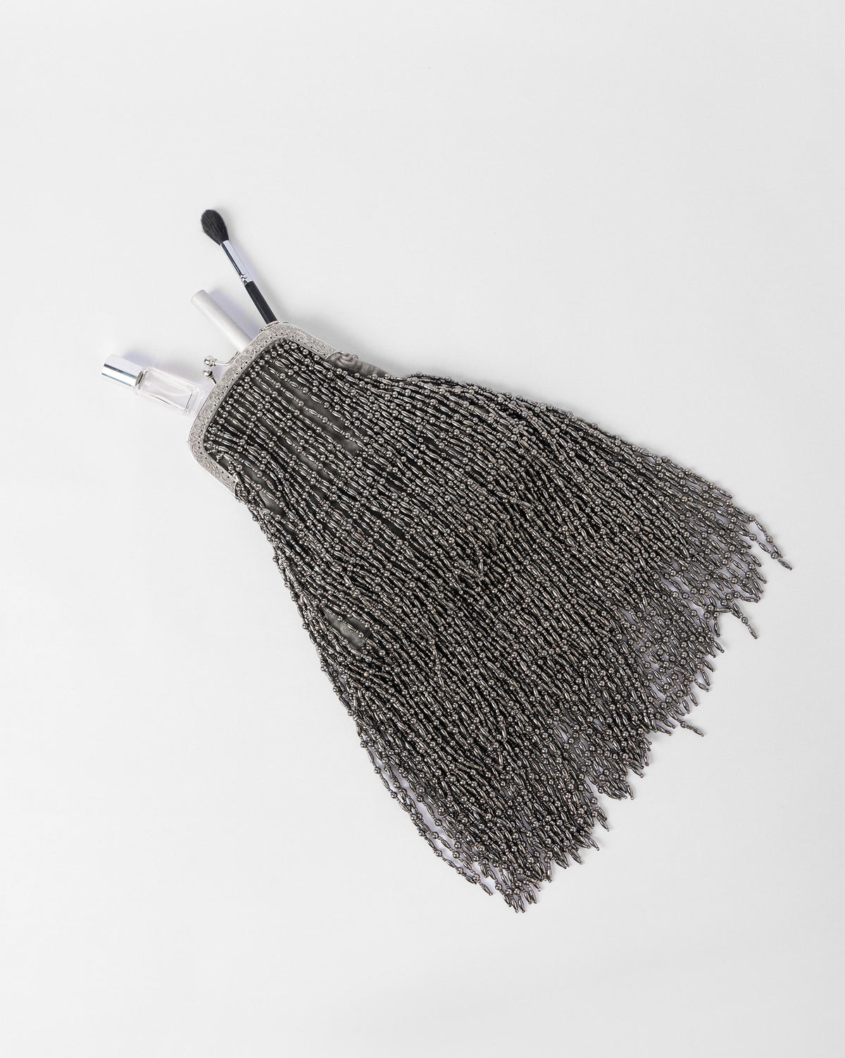 Silver beaded clutch held open with a brush, lipstick, and perfume inside.