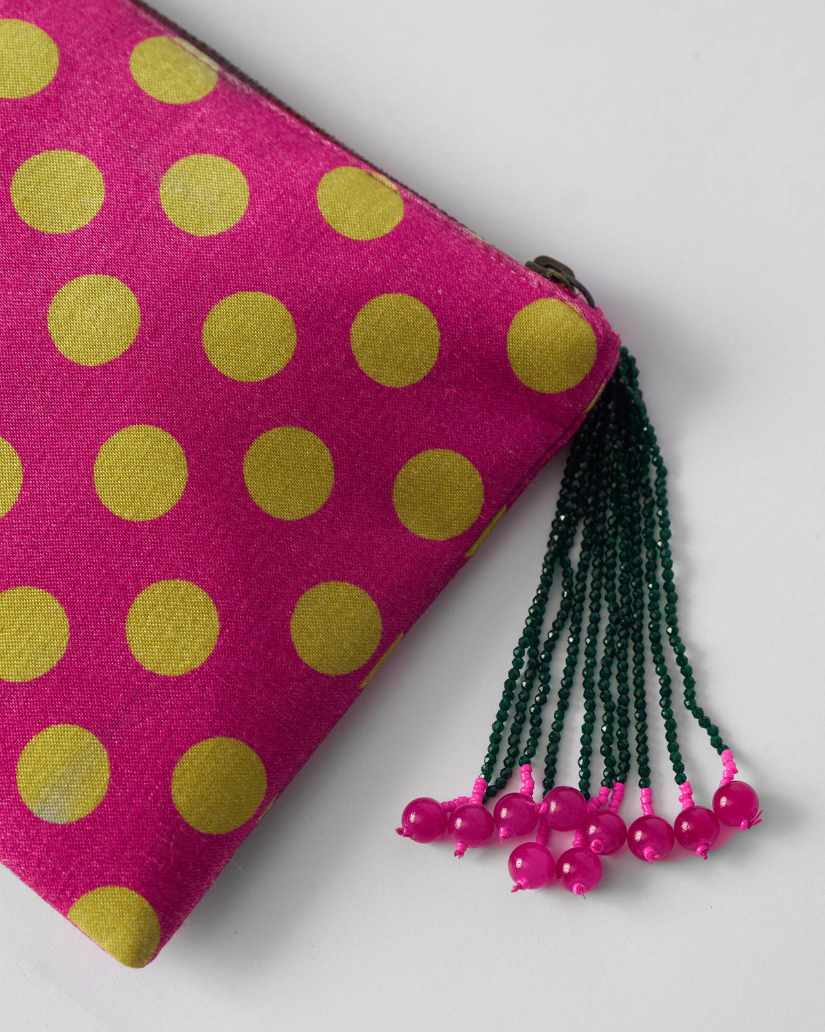 Close-up of a fuchsia polka pouch zipper with a dark green beaded tassel.