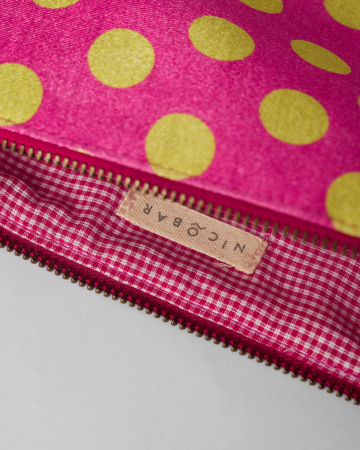 Open fuchsia polka pouch revealing pink gingham lining and a Nicobar label.
