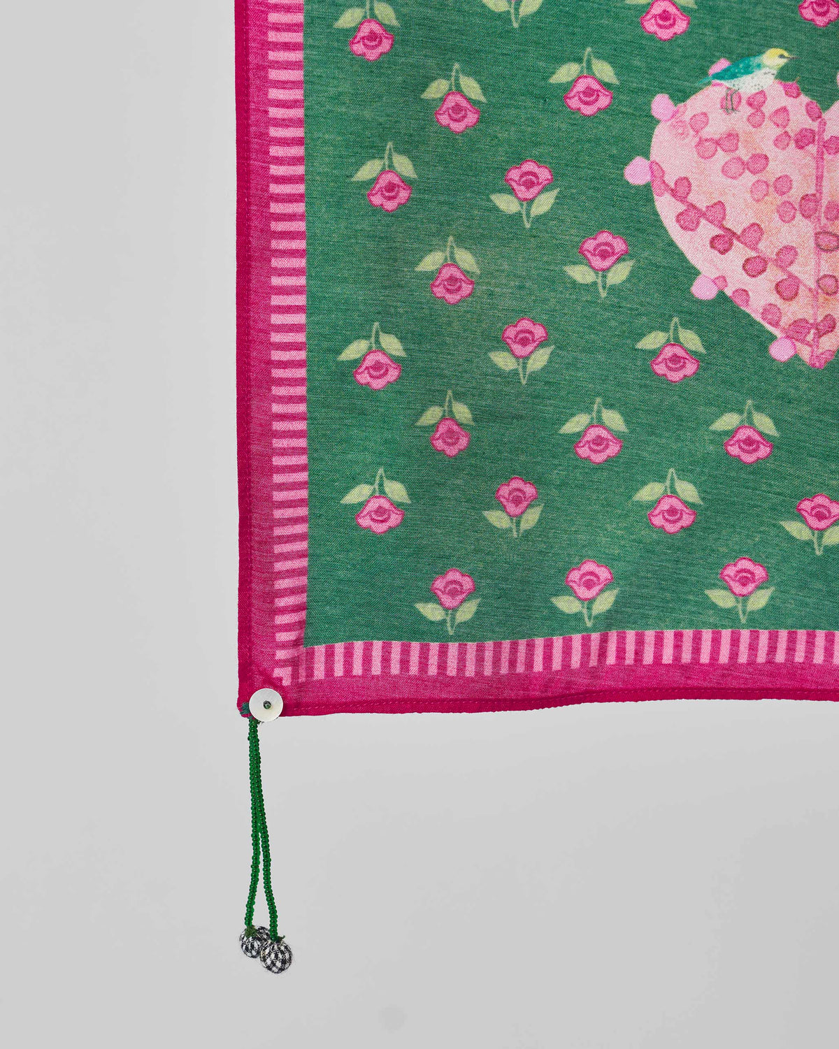 Close-up of a Gulnaar scarf corner showing pink flowers, a striped edge and a green tassel.