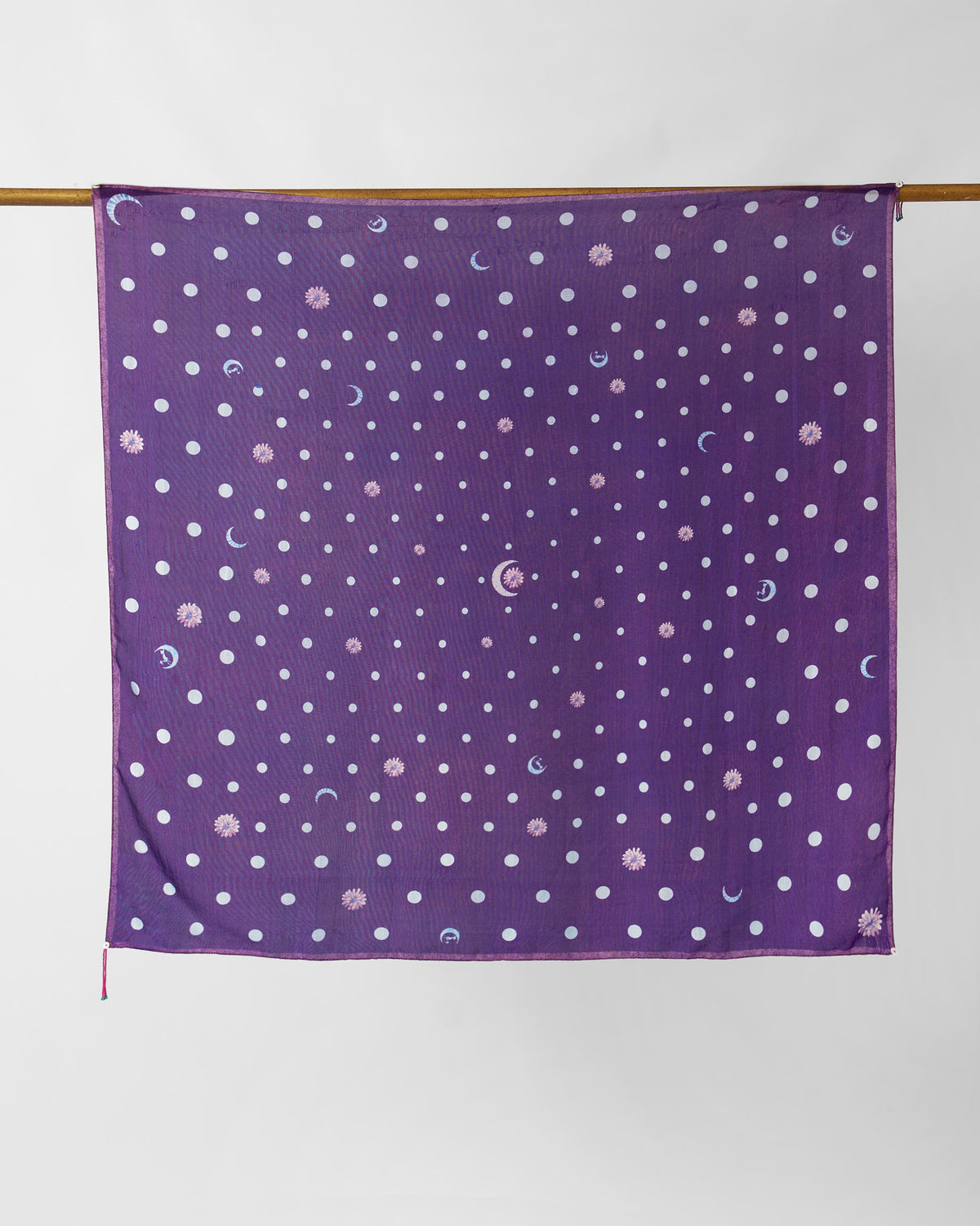 Purple silk scarf with white polka dots and moon motifs hung square on a rod.