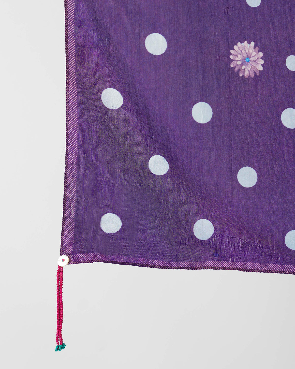 Close-up of a purple scarf corner with a pink beaded tassel and flower motif.