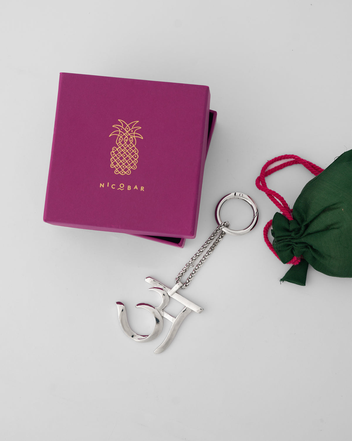 Alphabet A Bag Charm in silver beside a magenta Nicobar gift box and green pouch.